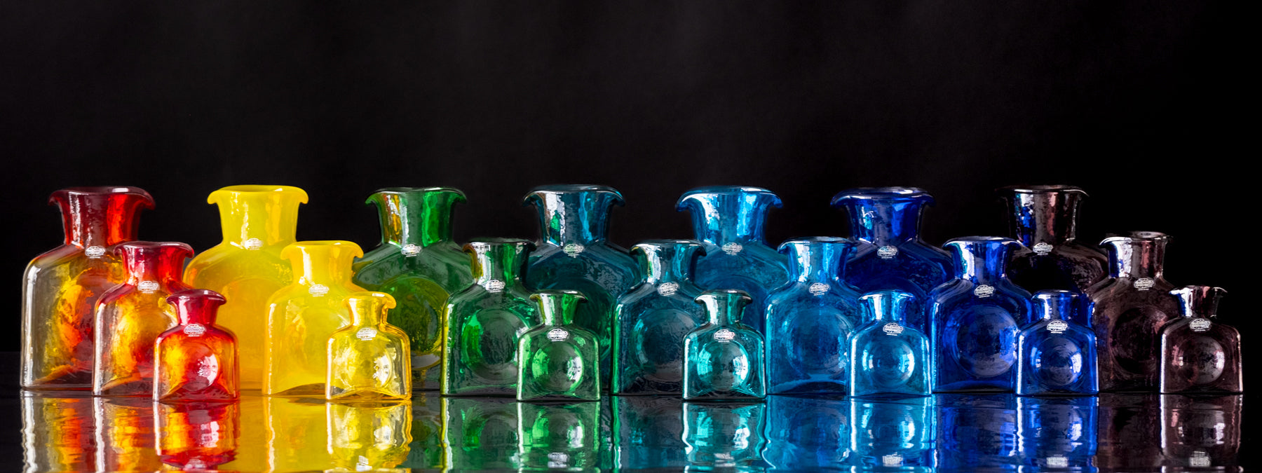 Colorful glass bottles arranged in a row on a reflective surface with a black background