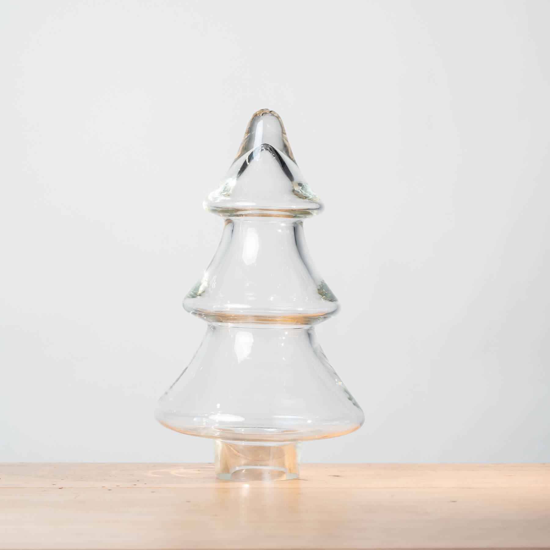 Clear glass Christmas tree-shaped object on a light wooden surface with a light gray background