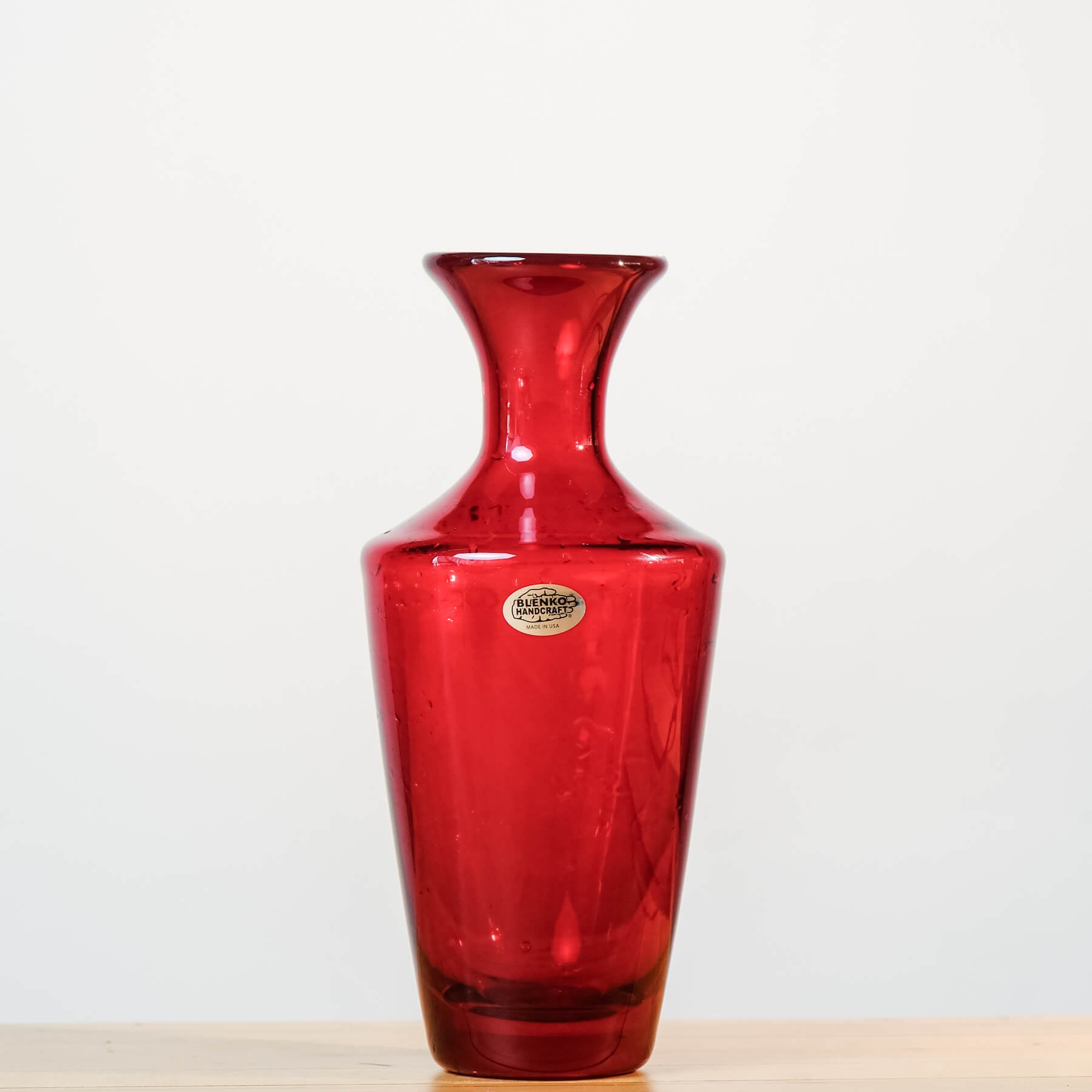 Red glass vase with a visible brand label on a light background