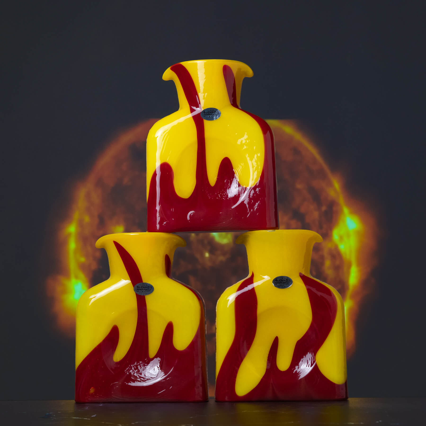 Three ceramic vases with red and yellow glaze stacked on a dark background