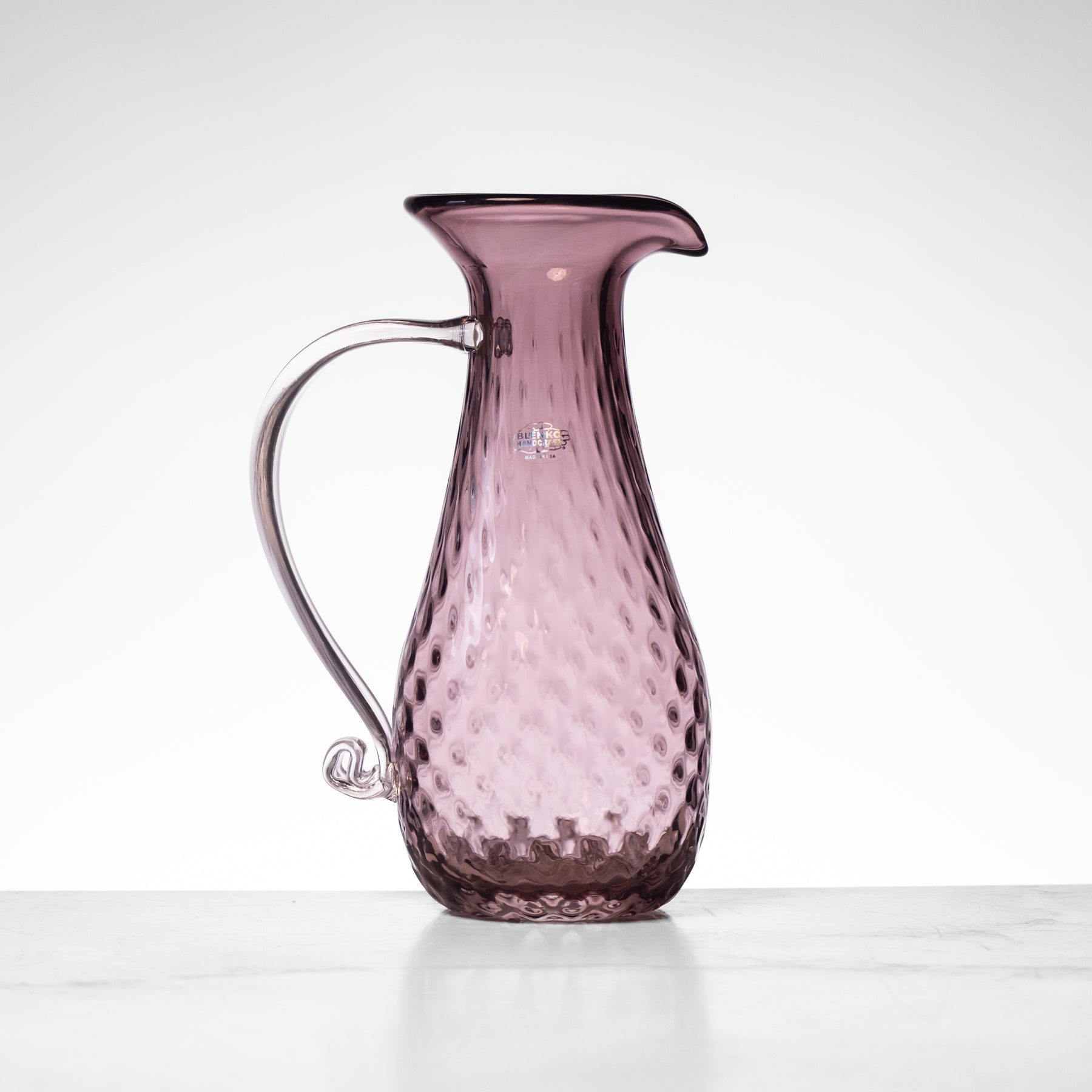 Pink glass pitcher with textured surface on a white background