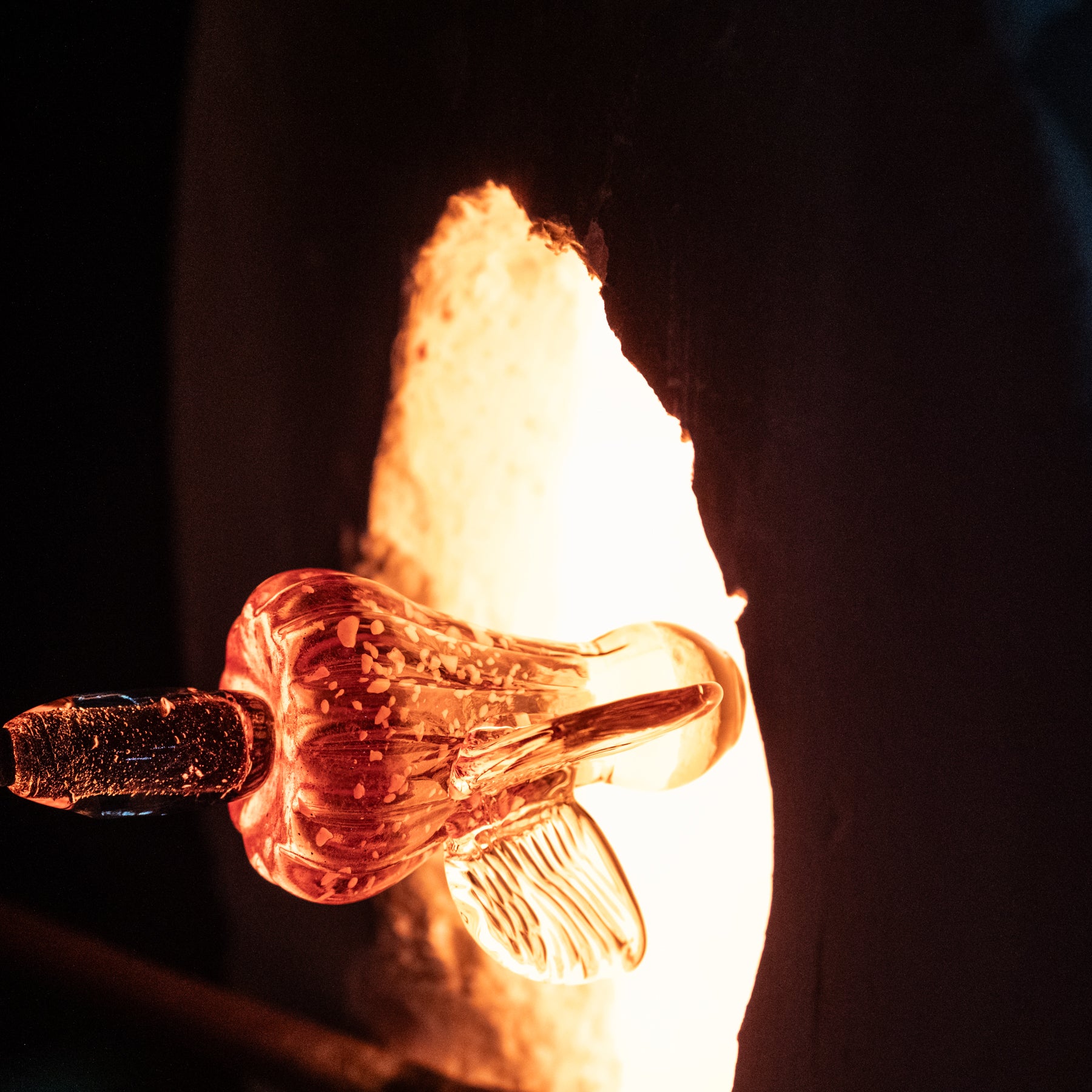 Close-up of a glassblowing process with molten glass and tools.