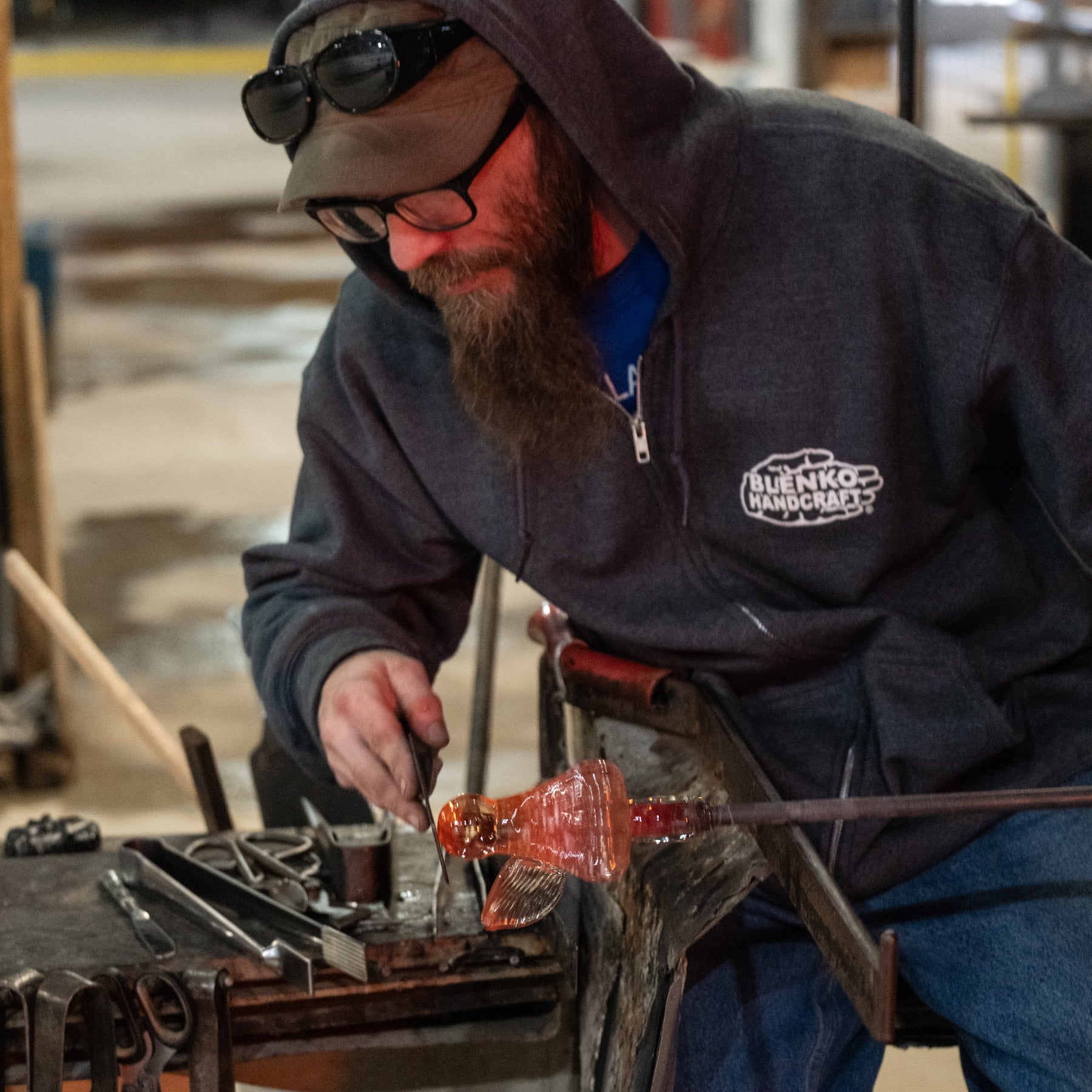 Person working with metal in a workshop, wearing a hoodie with a visible brand logo.
