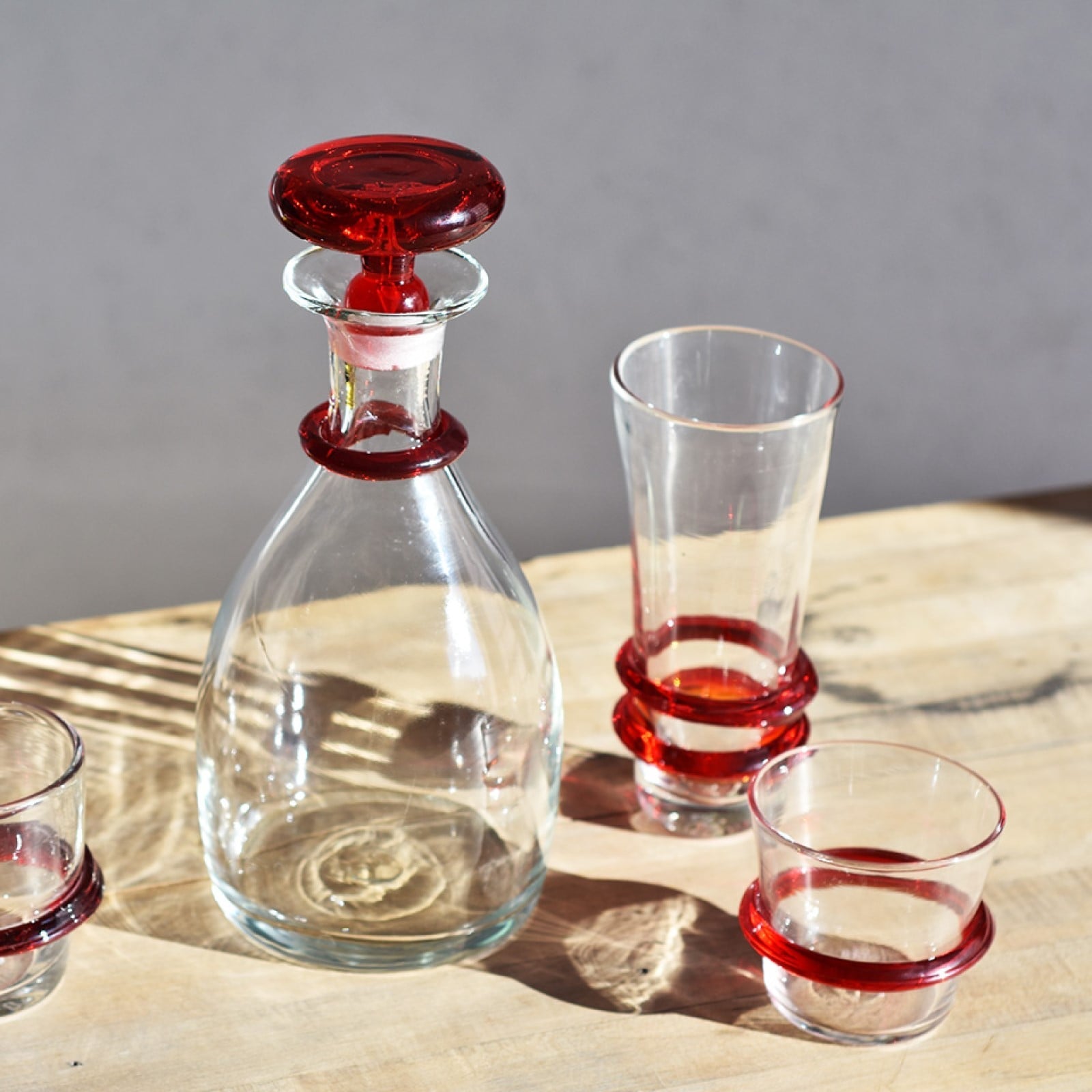 Clear glass decanter with red stopper and three matching glasses on a wooden surface.