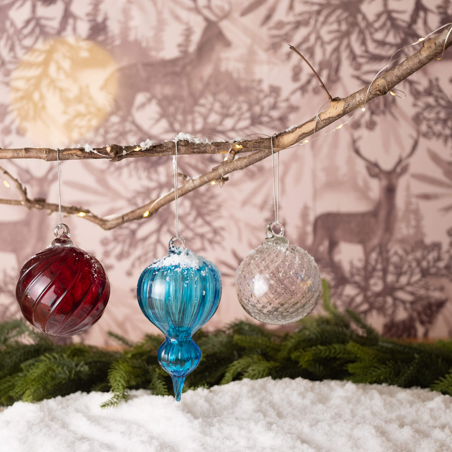 Three glass ornaments hanging from a branch with a festive background