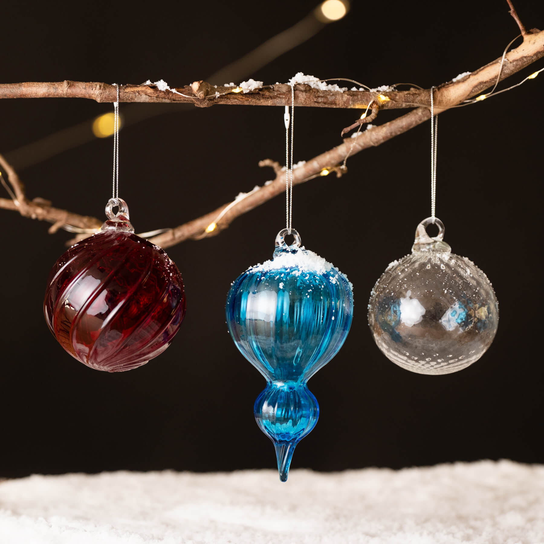 Three glass ornaments hanging from a branch with a dark background