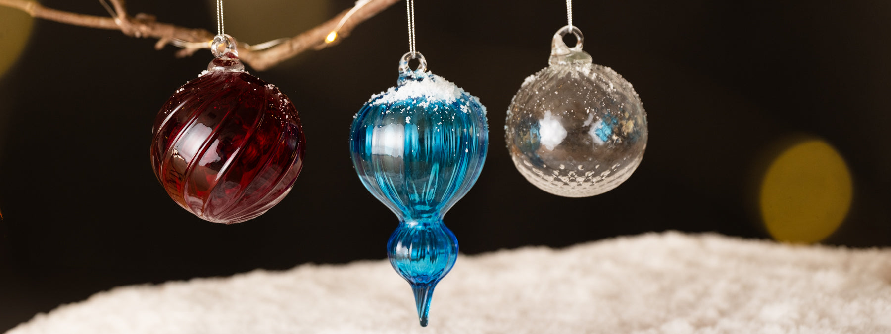Three glass ornaments in red, blue, and clear on a snowy surface with a dark background.