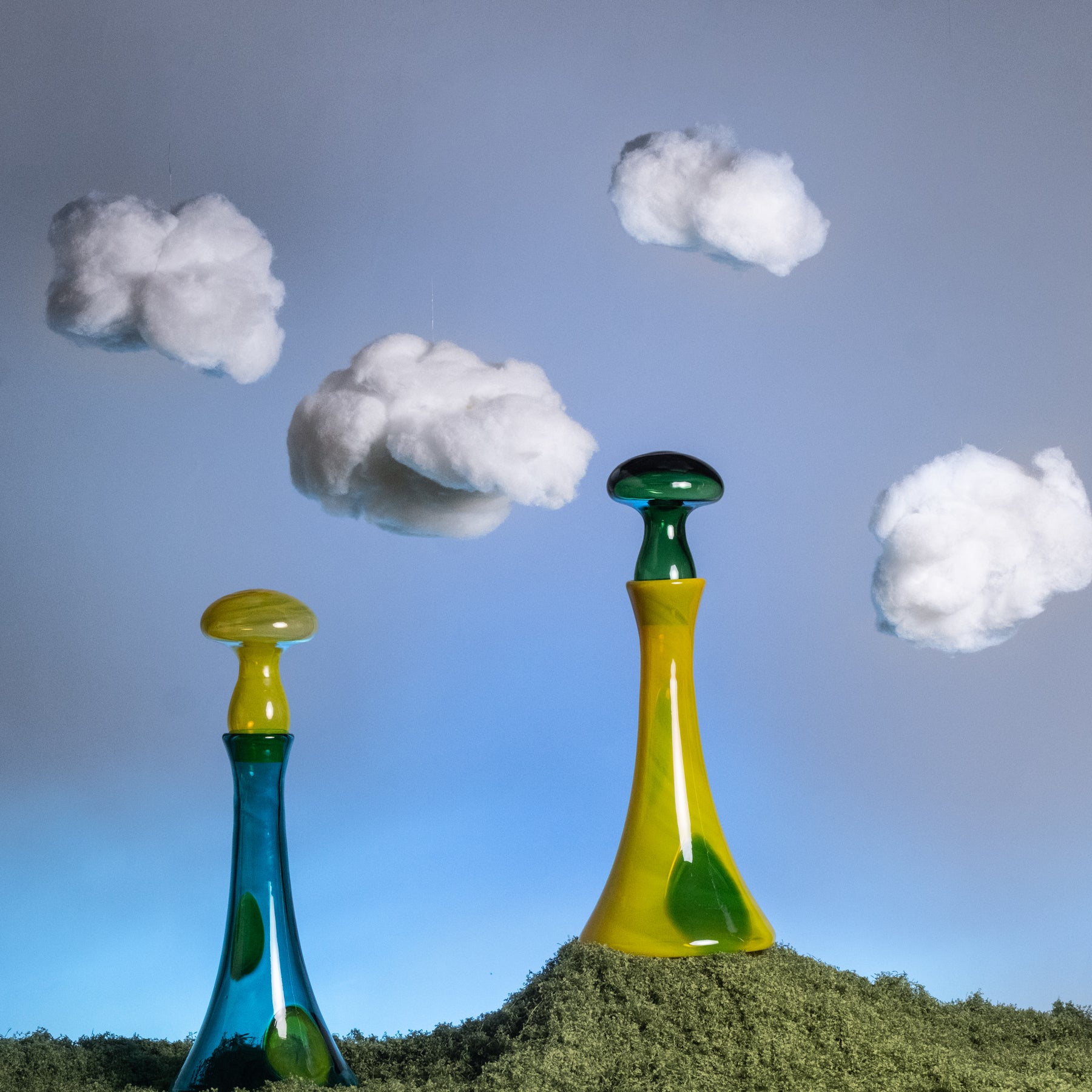 Two colorful glass bottles on a grassy hill with clouds in the sky