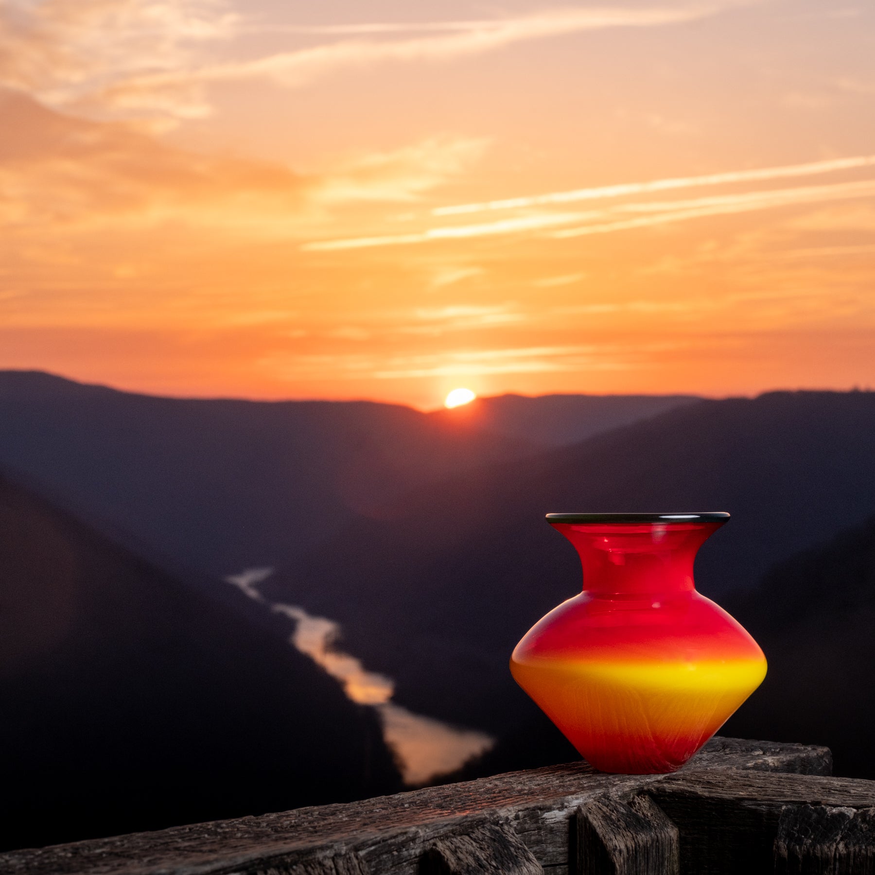 Red and yellow vase on a wooden surface with a mountain landscape and sunset in the background