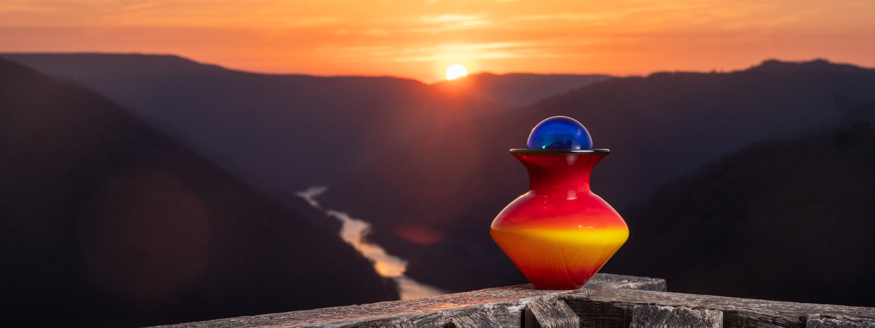 Red and yellow vase on a wooden surface with a mountain landscape and sunset in the background