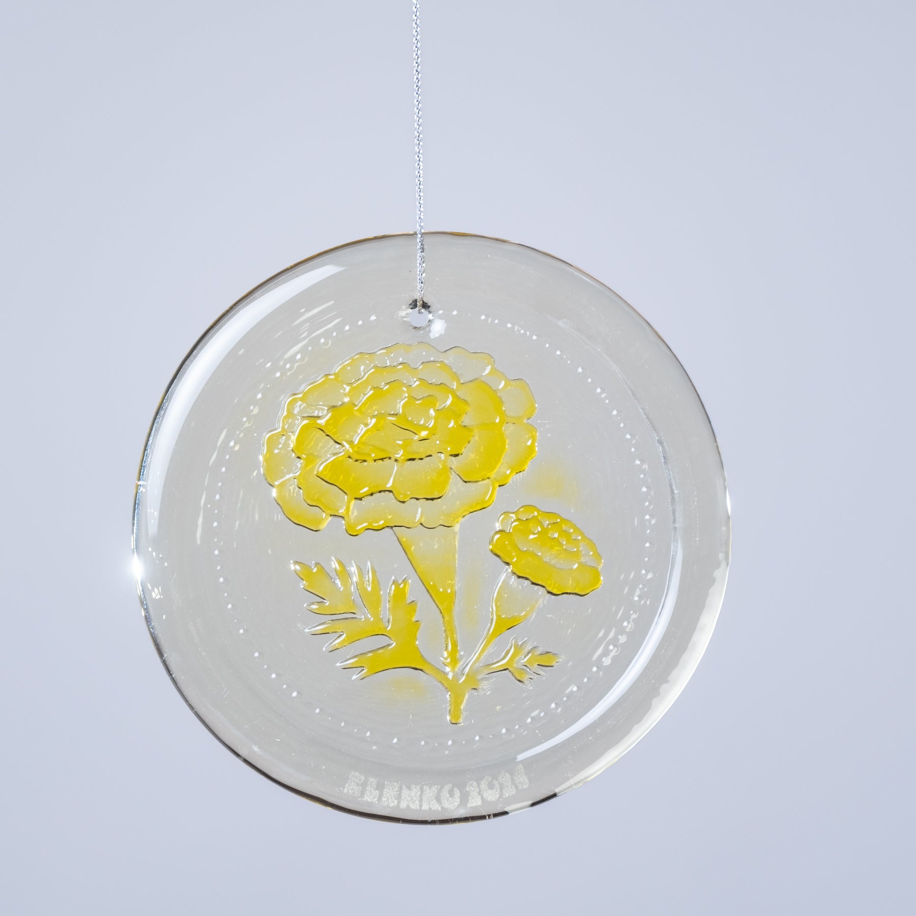 Round clear glass ornament with yellow floral design on a light gray background