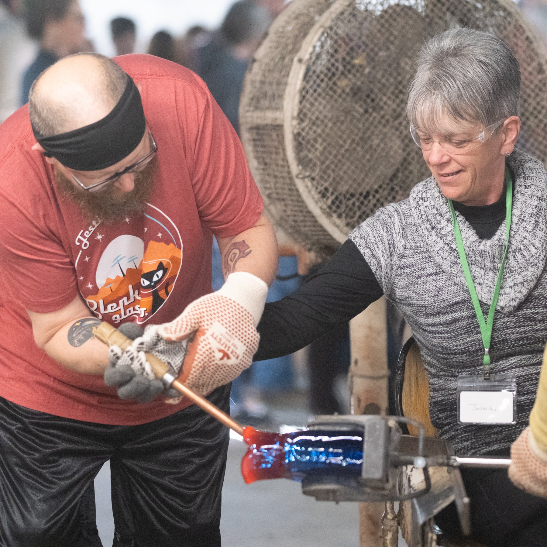 Two people working with glassblowing tools at a glass blowing event.
