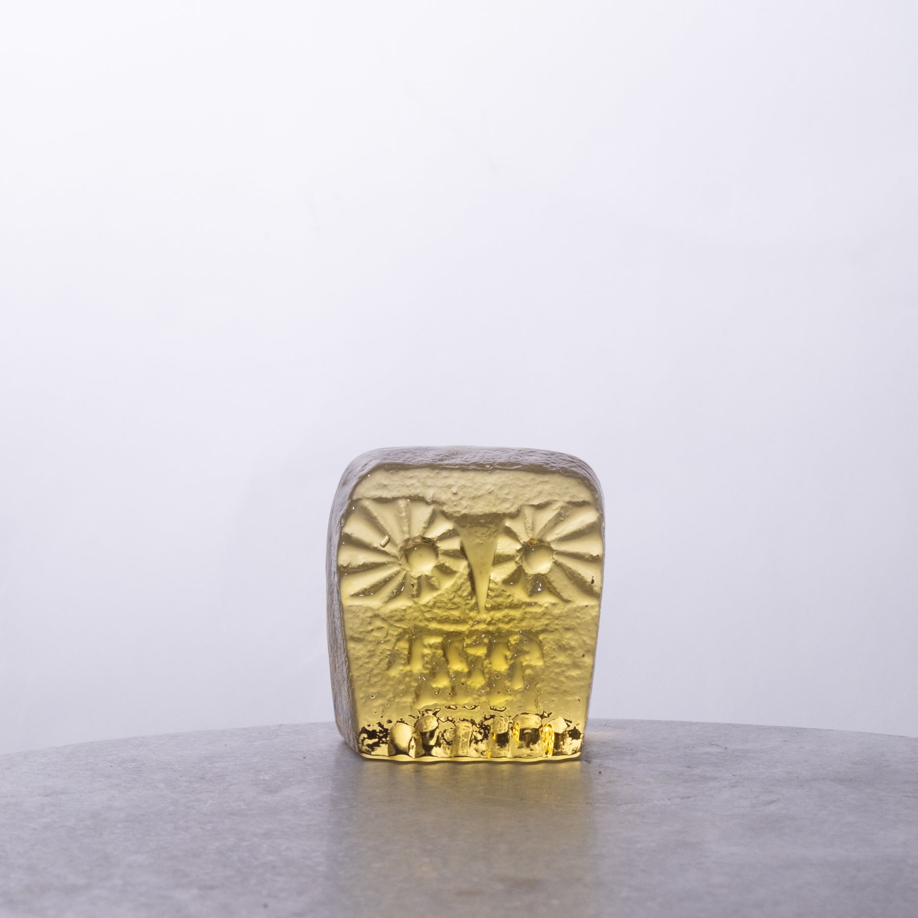 Gold ingot on a reflective surface with a light gray background
