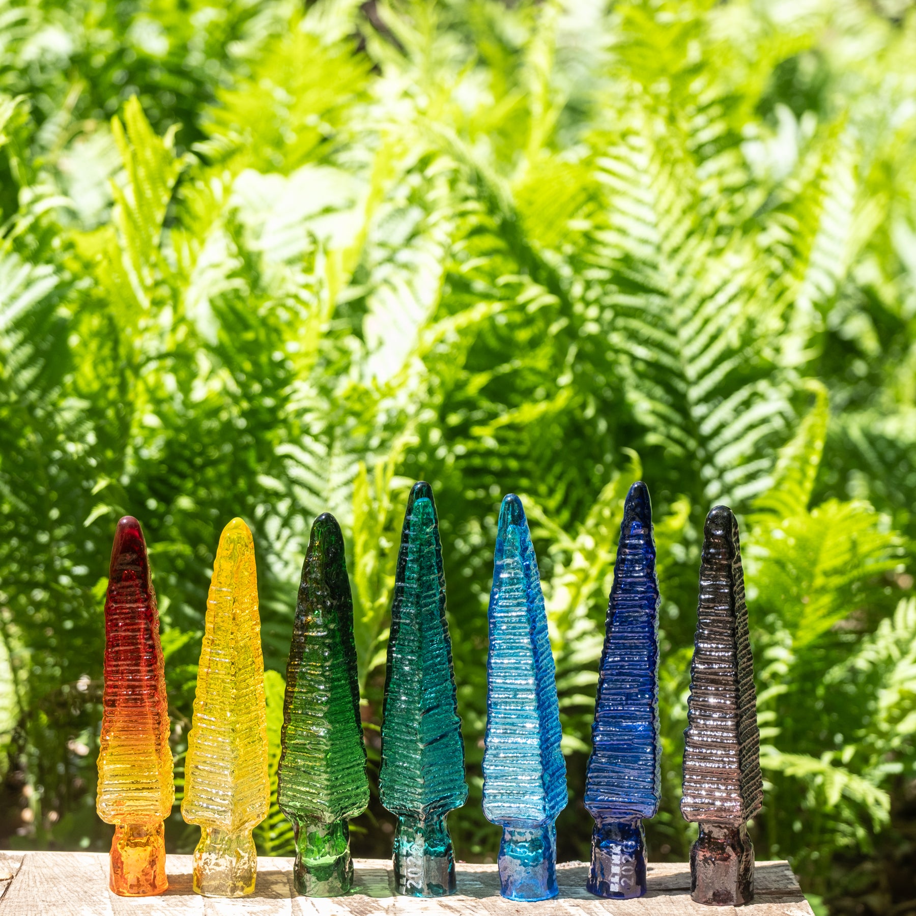 Set of colorful glass trees against a green fern background