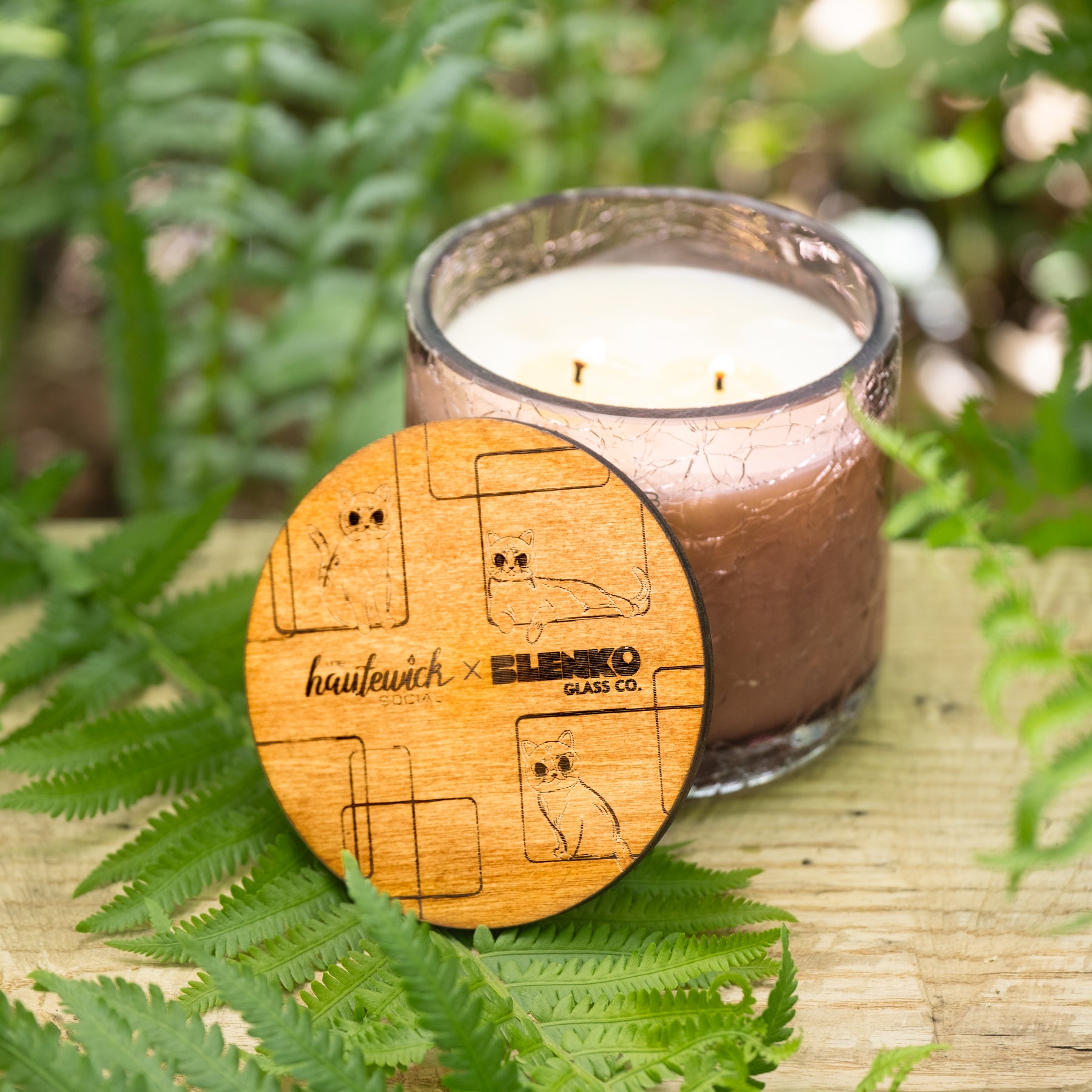 Candle with wooden coaster featuring 'hautefevich x ELENKO' branding on a natural background