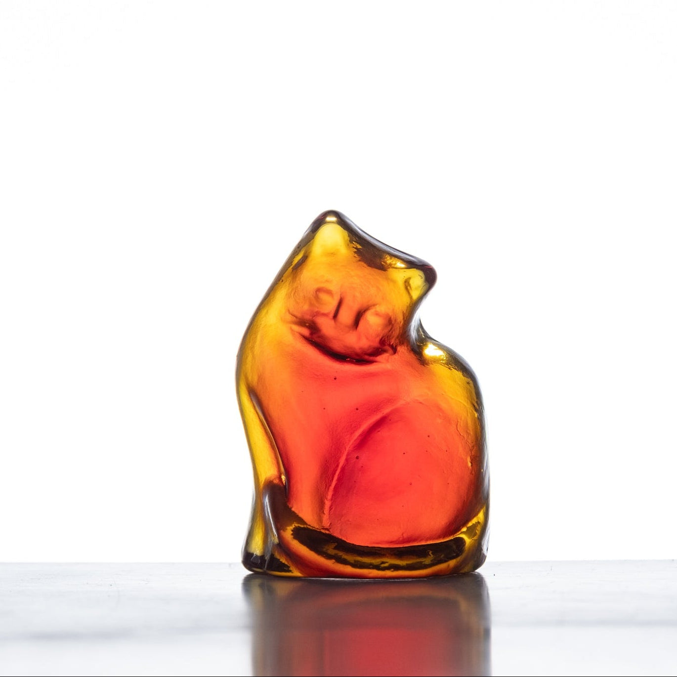 A handcrafted glass figurine of a cat with a tangerine orange color, showing a whimsical and playful design.