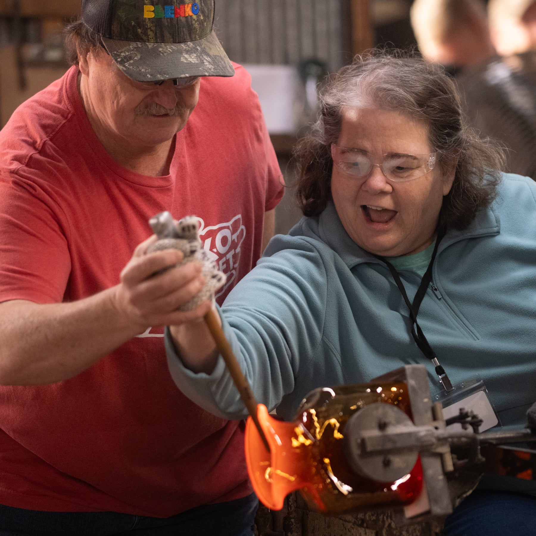 Two people working with glassblowing tools in a workshop setting.