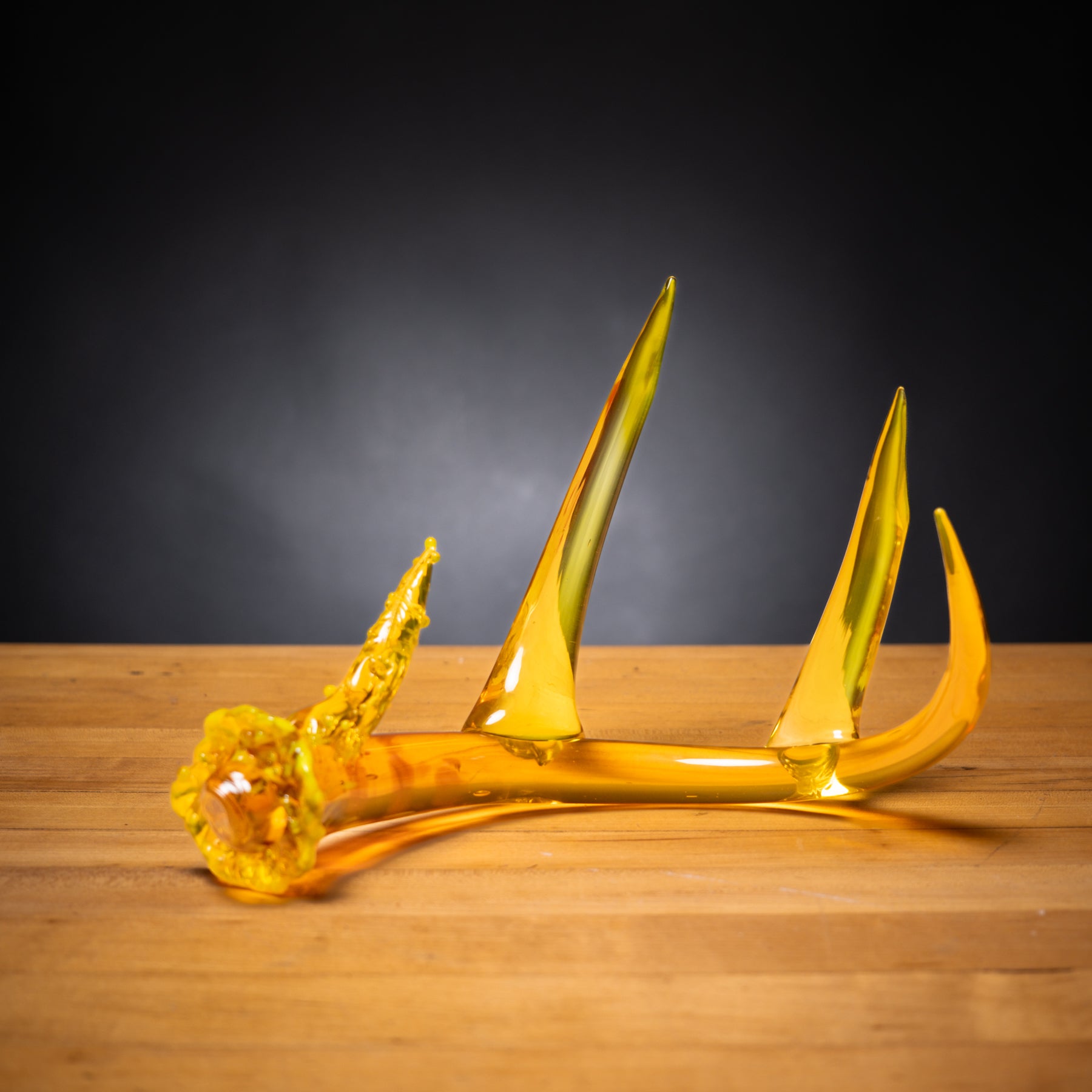 Yellow glass sculpture on a wooden surface with a dark background