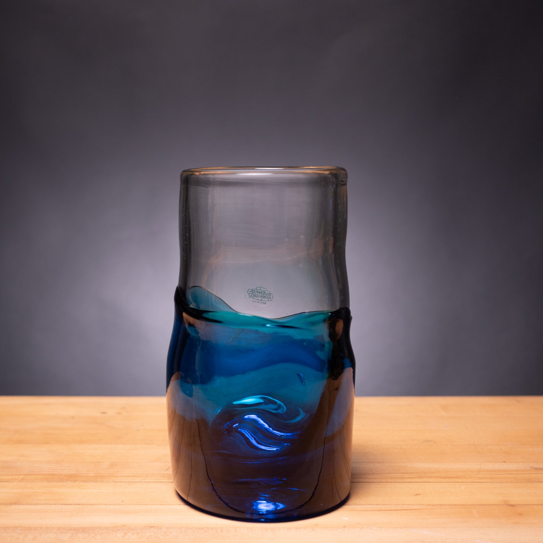 Glass vase with blue interior on a wooden surface against a gray background