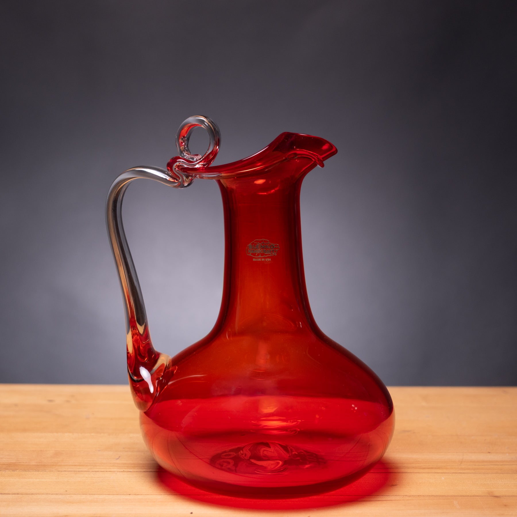 Red glass decanter on a wooden surface with a dark gray background