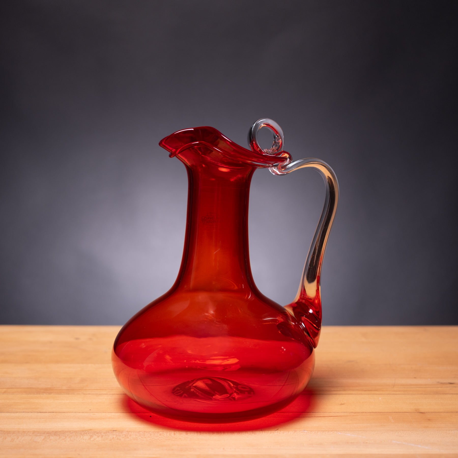 Red glass decanter on a wooden surface with a dark background