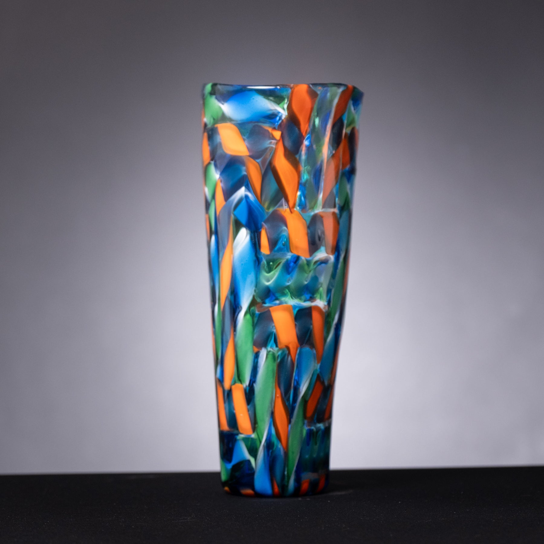 Colorful glass vase with blue, orange, and green patterns on a gray background