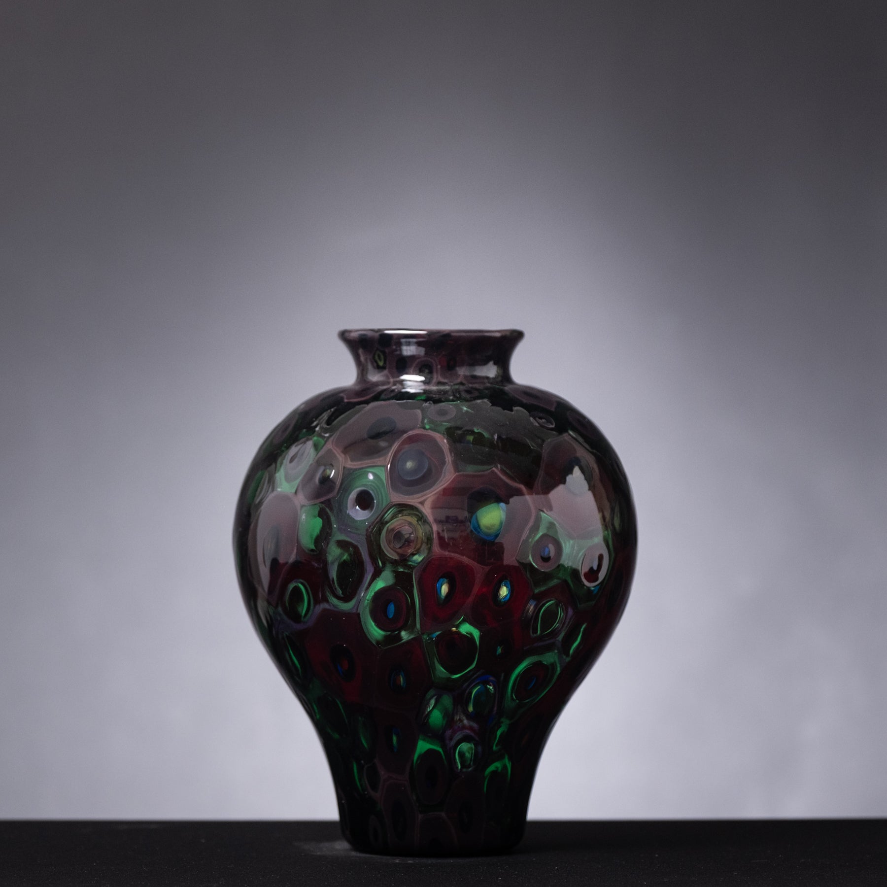 Decorative glass vase with a dark, textured surface on a gray background
