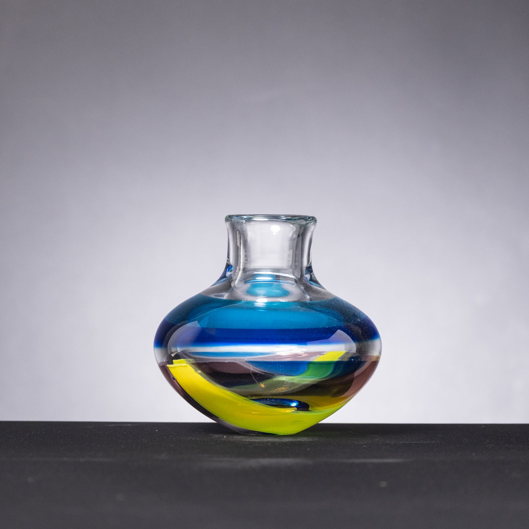 Colorful glass vase with blue and yellow stripes on a gray background