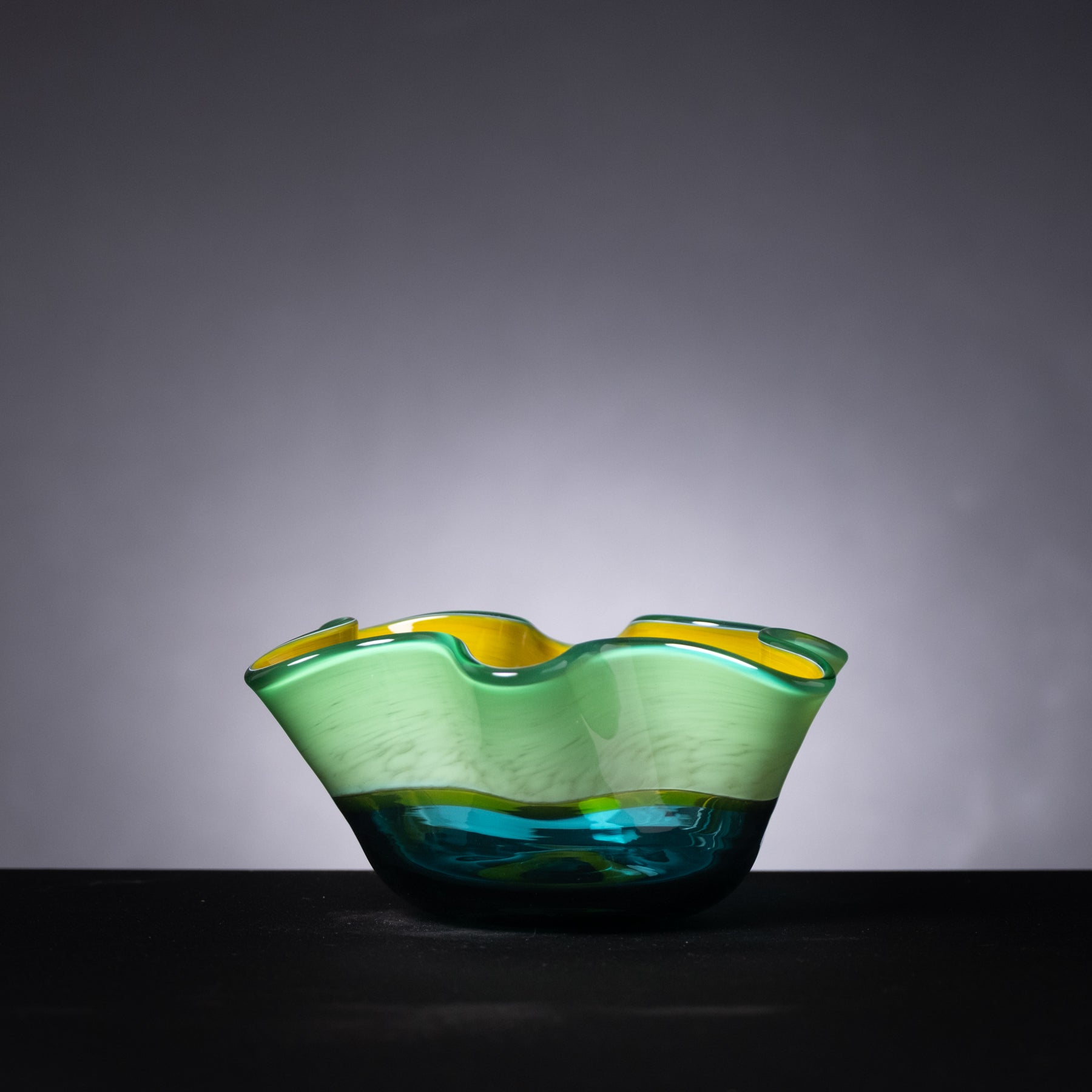 Green and blue glass bowl on a dark surface with a gray background