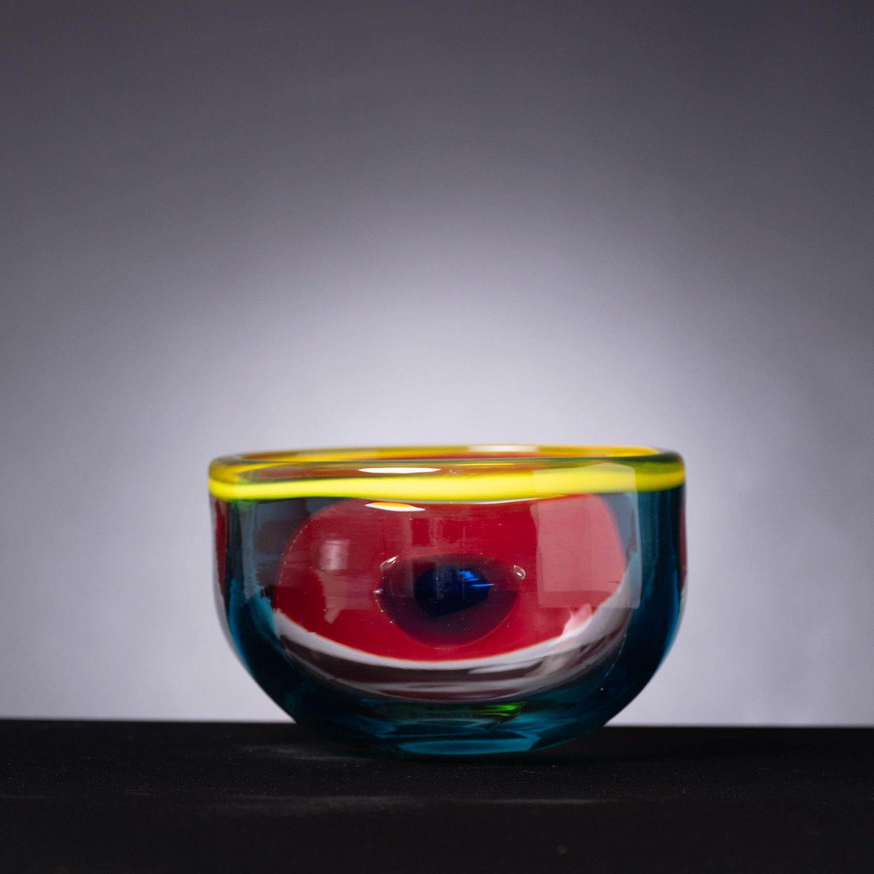 Colorful glass bowl with a gradient of red, yellow, and blue on a dark background