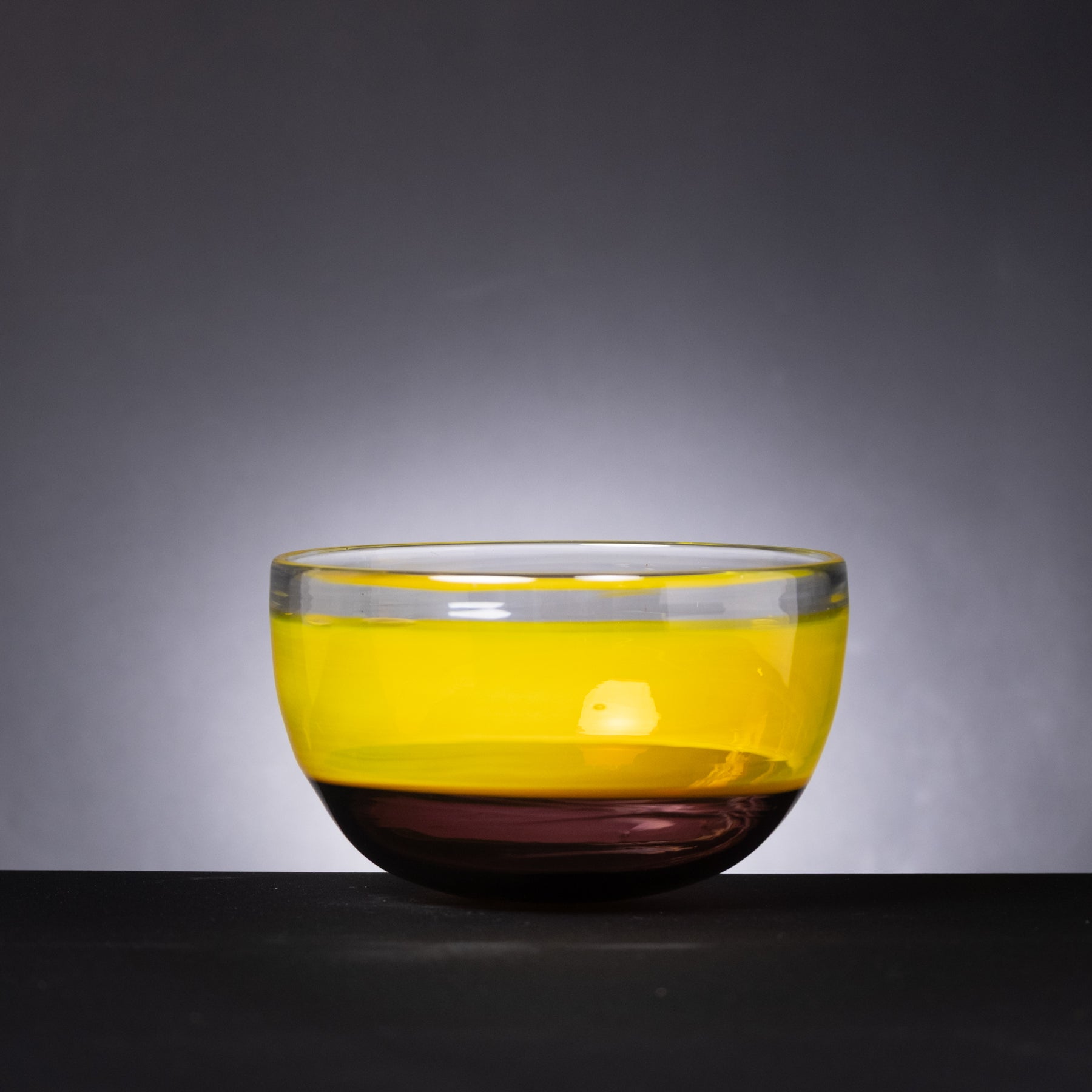 Glass bowl with yellow top and dark base on a gray background