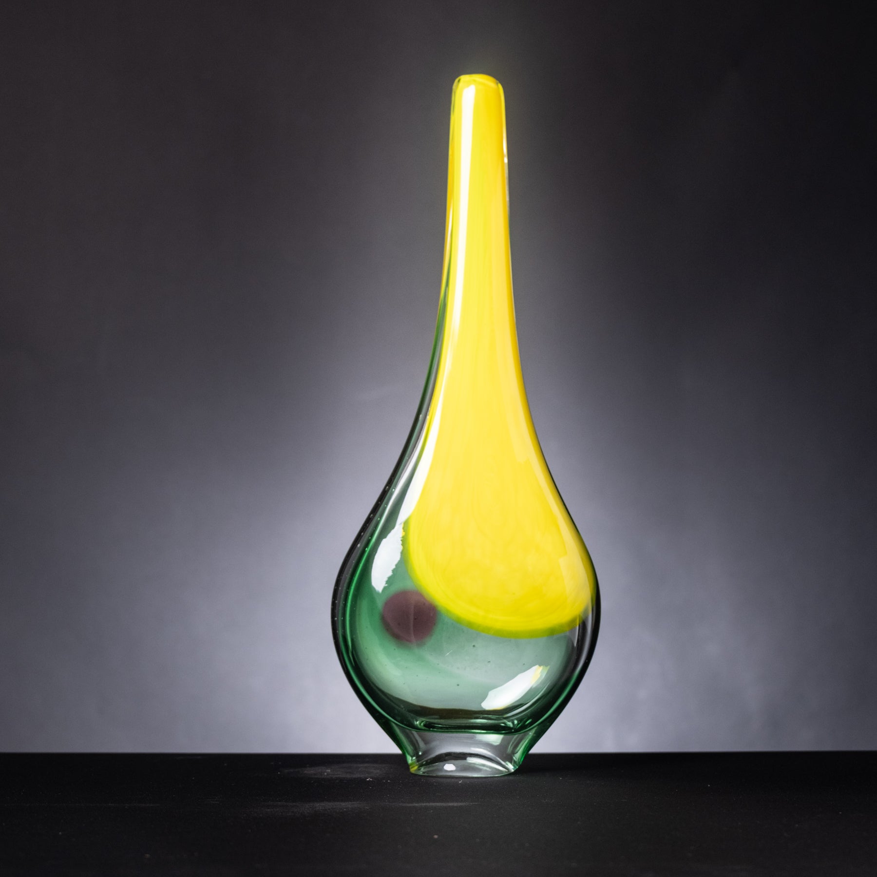 Glass vase with yellow top and green base on a dark background