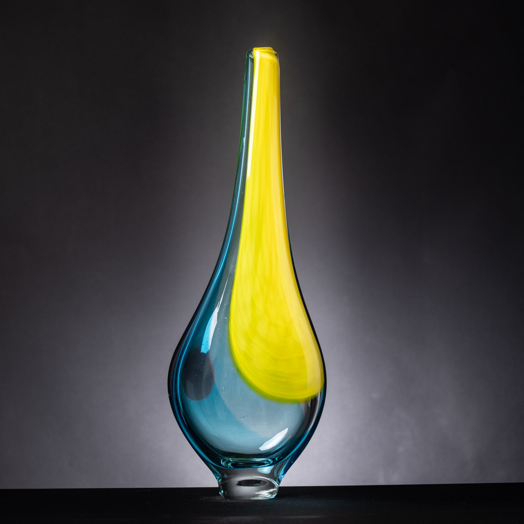 Glass vase with a yellow top and blue base on a dark background