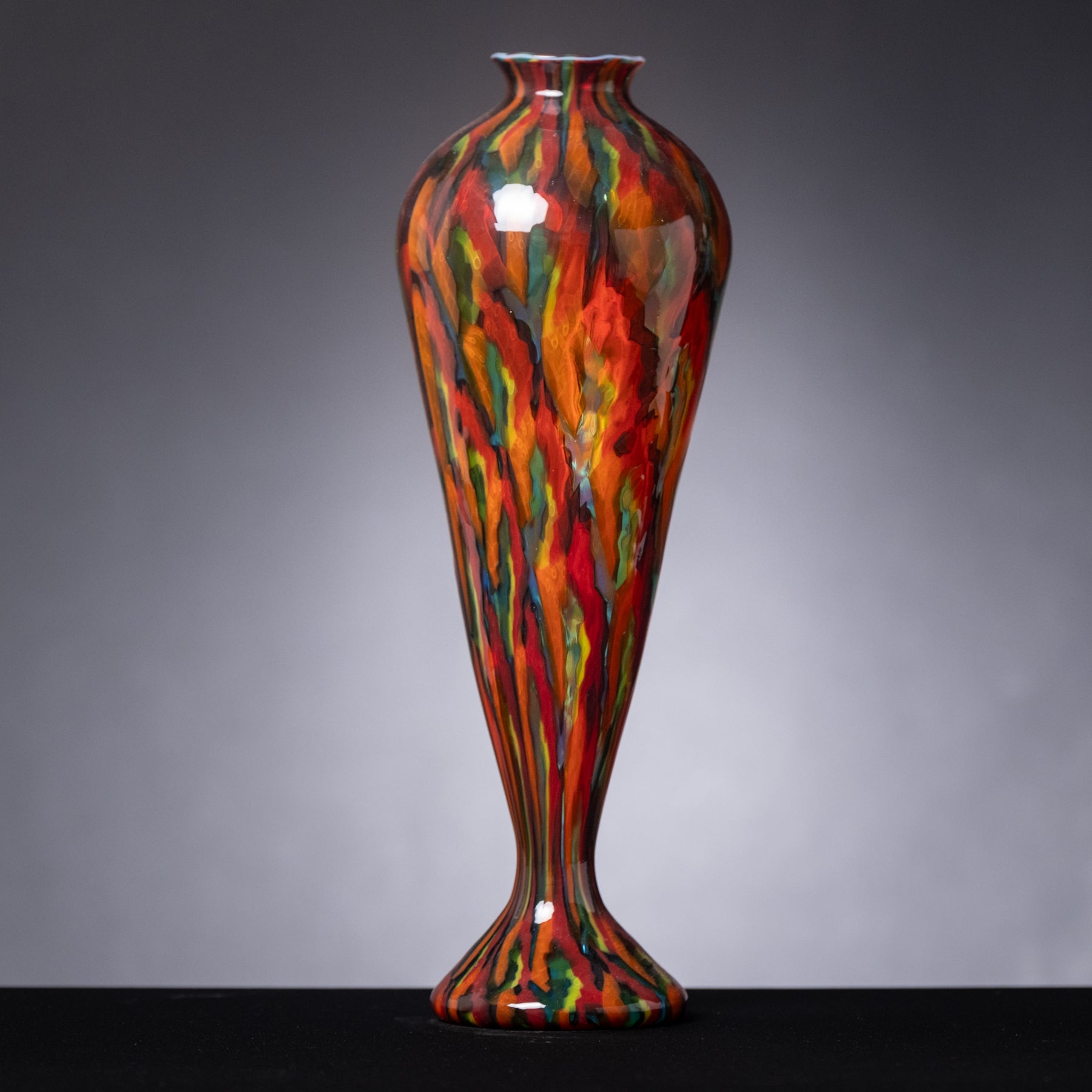 Colorful glass vase with flame-like patterns on a gray background