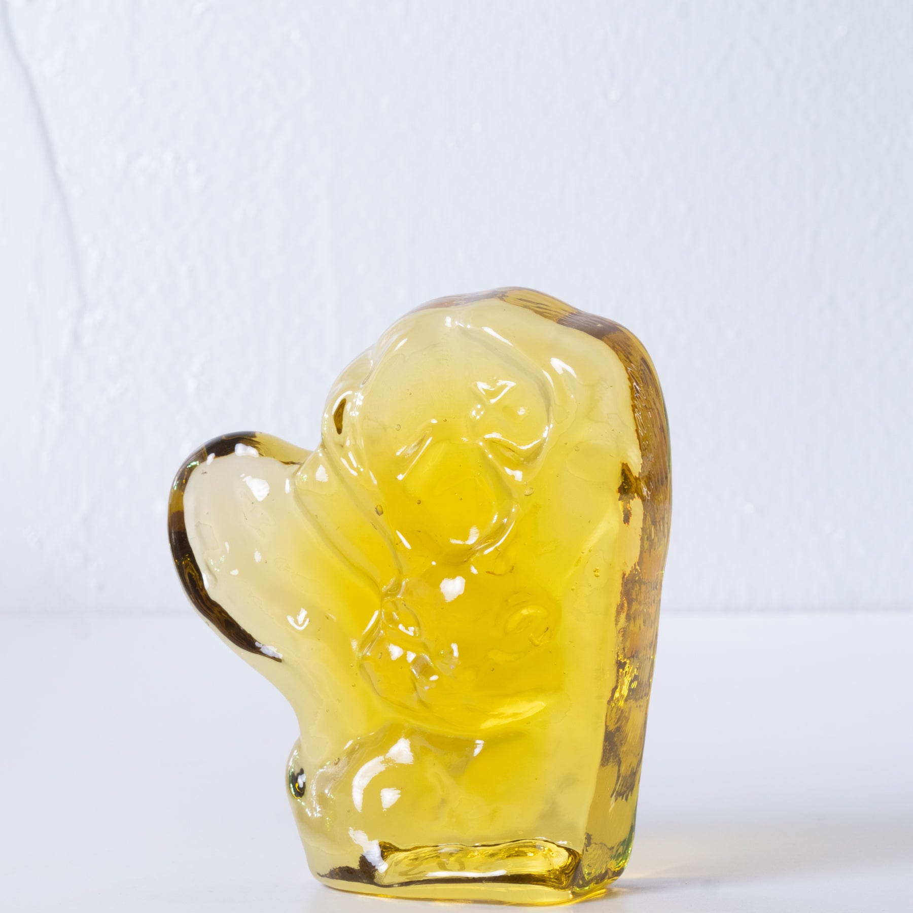 Yellow glass figurine of a seated figure on a white background