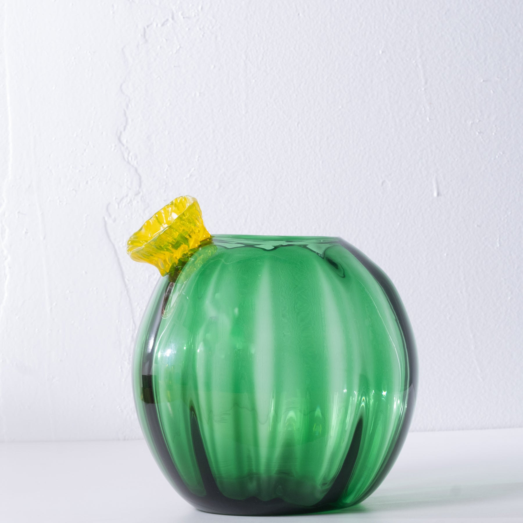 Green glass cactus with yellow flower on white background.