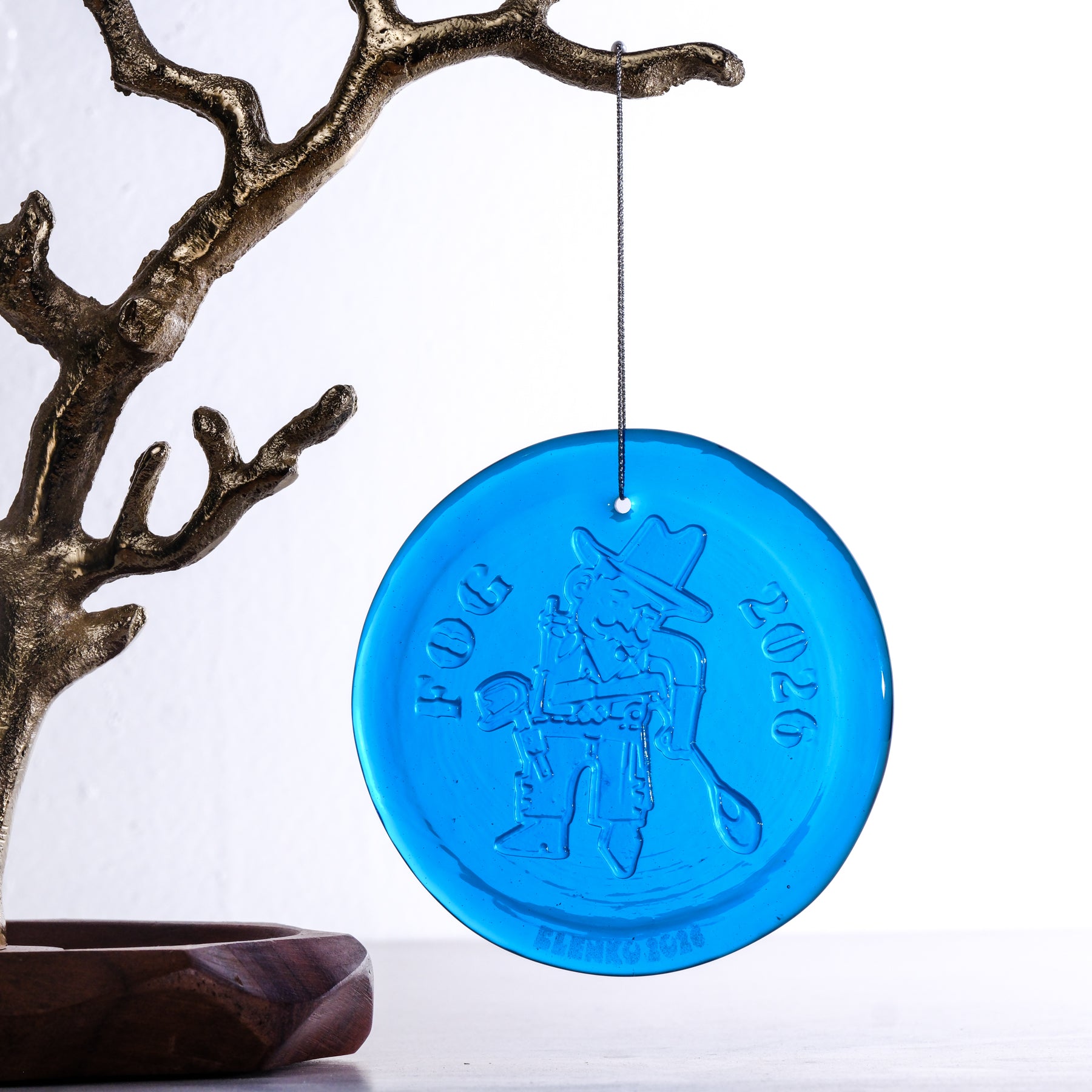 Turquoise round glass object hanging from branch on white background