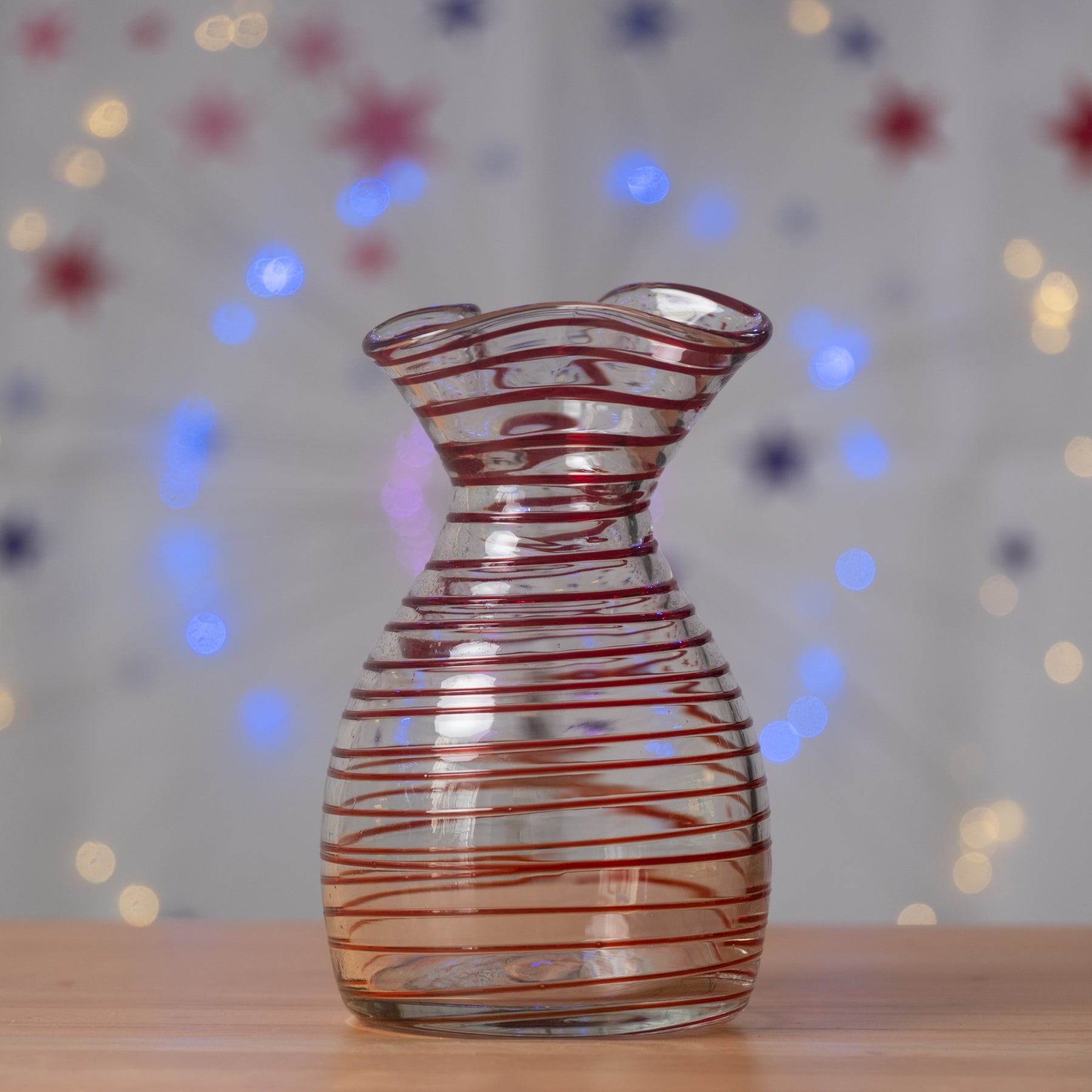 Glass vase with red swirls on a wooden surface with a blurred colorful background