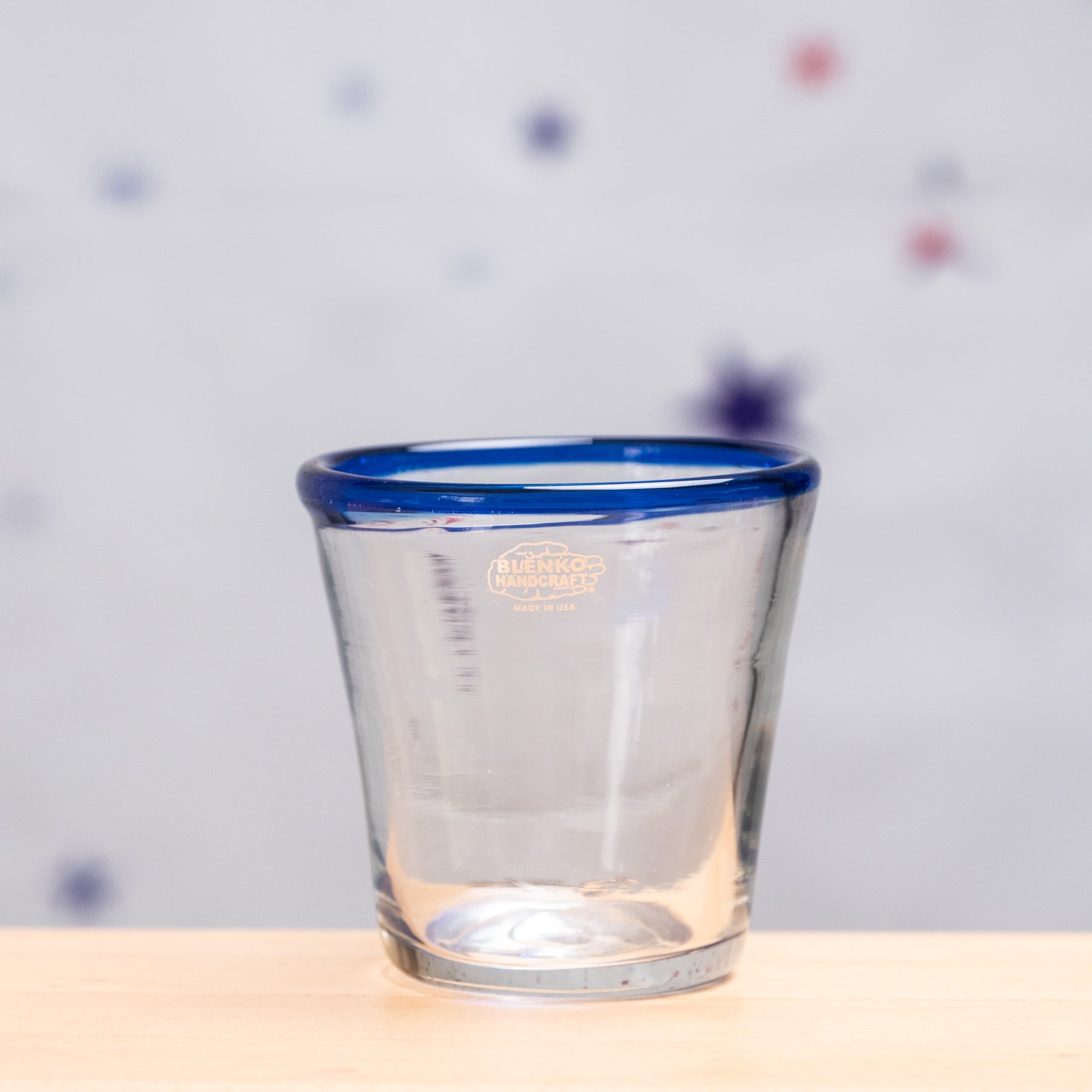 Clear glass with blue rim on a wooden surface and polka dot background