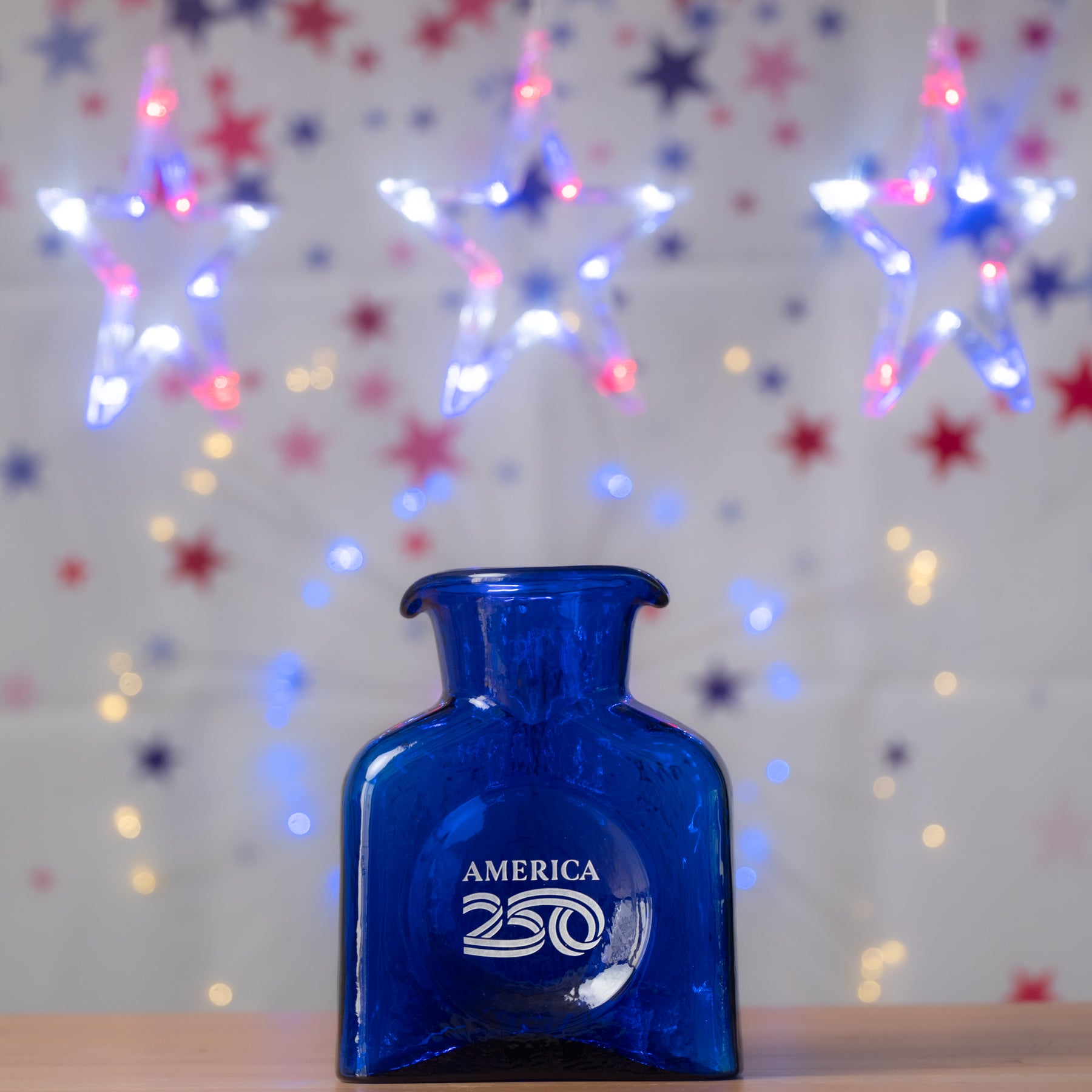 Blue bottle labeled 'America 250' with festive lights in the background