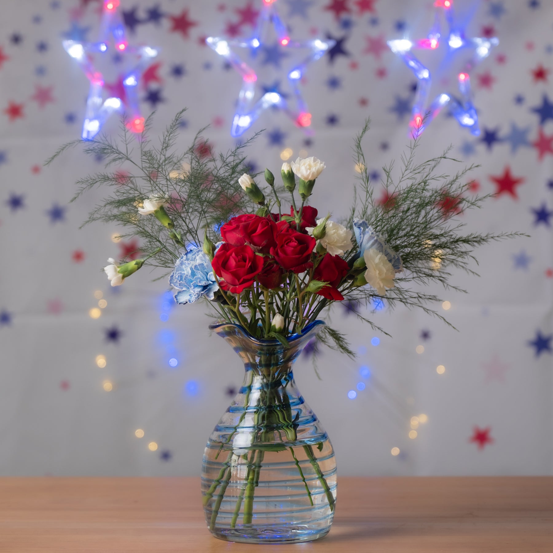 Bouquet of red and white flowers in a clear vase with colorful star lights in the background