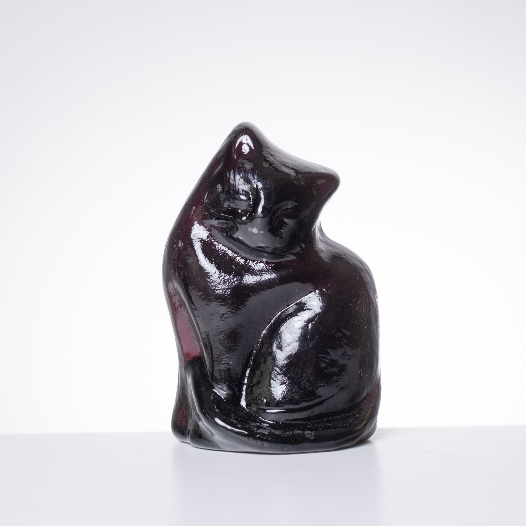 A glossy, dark reddish-black cat figurine sitting upright, photographed against a clean white studio background.