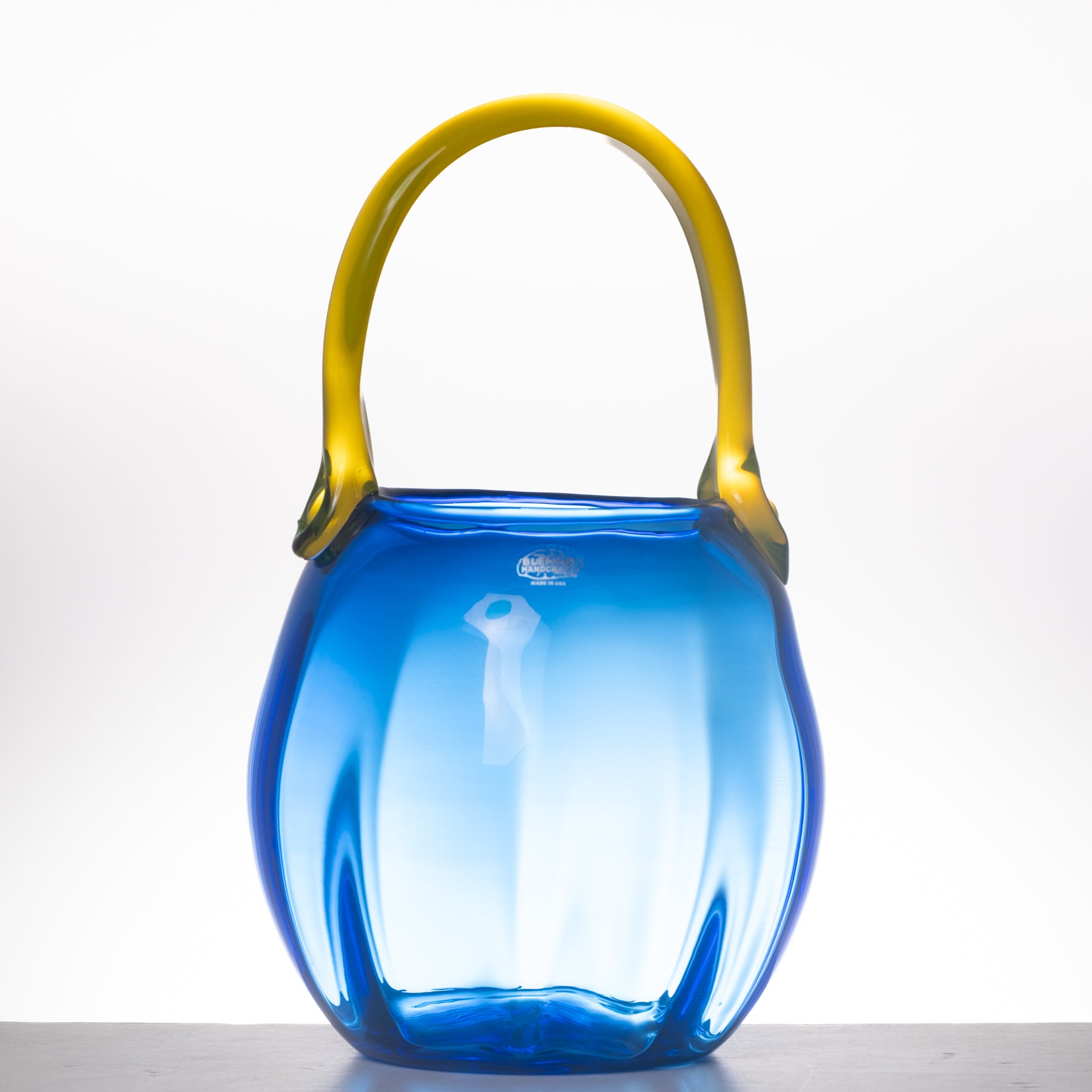 A translucent blue glass handbag with a curved yellow handle, photographed against a clean white studio background.