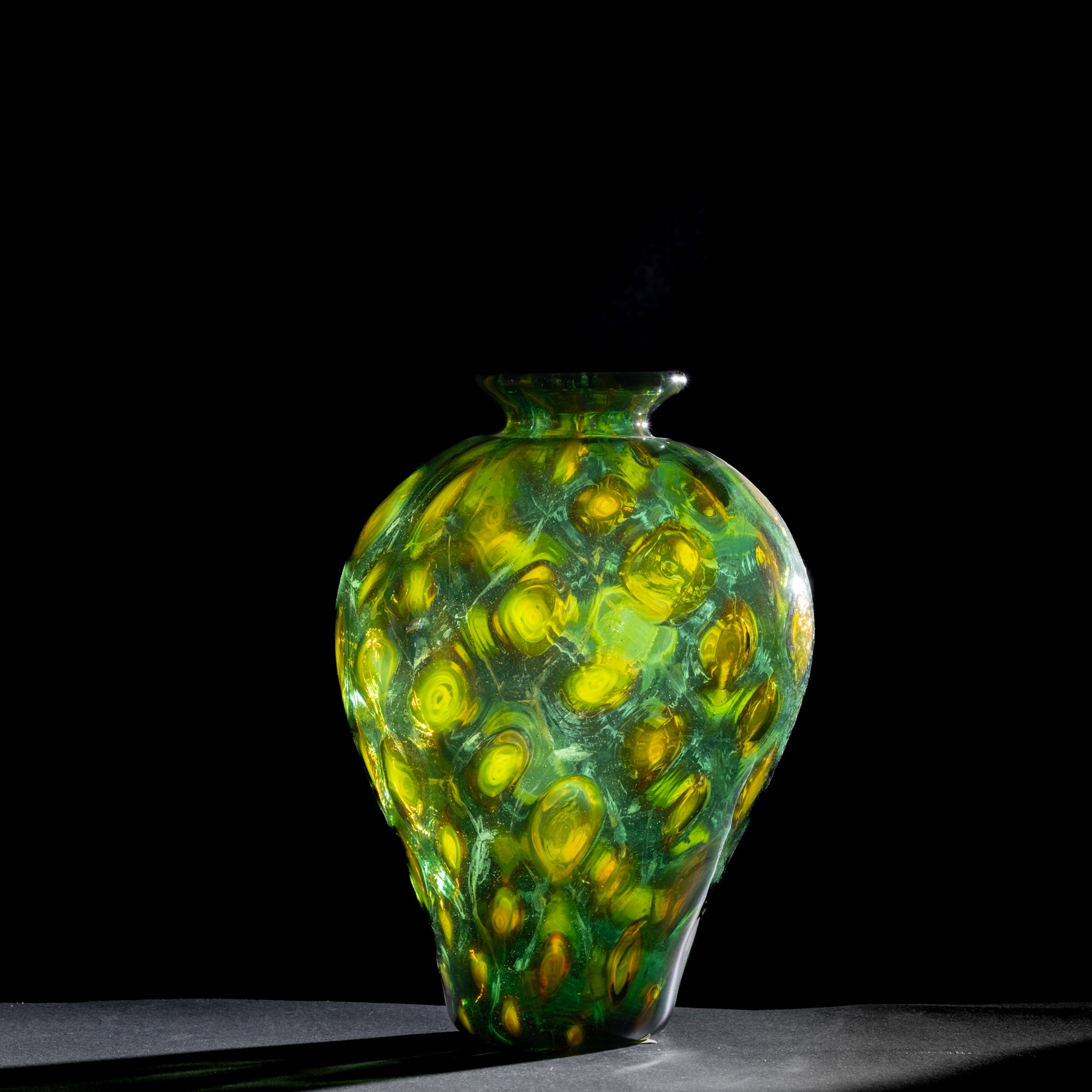 Green and yellow glass vase on a black background