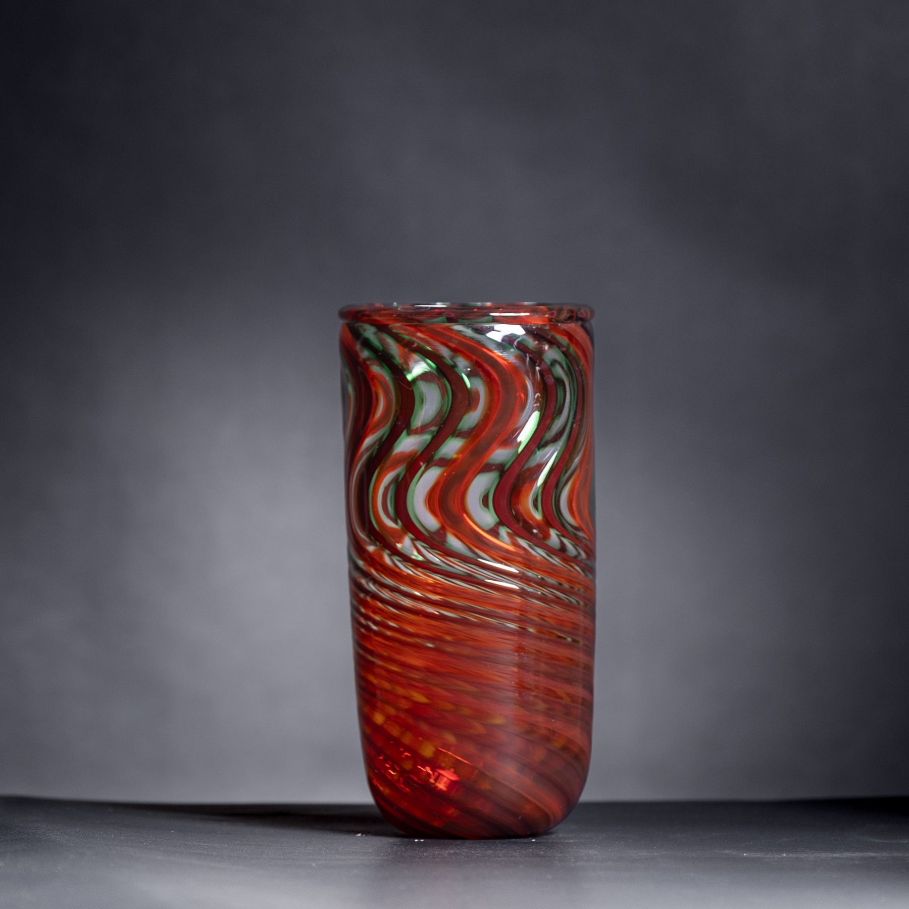 Glass vase with red and green swirl pattern on a dark background