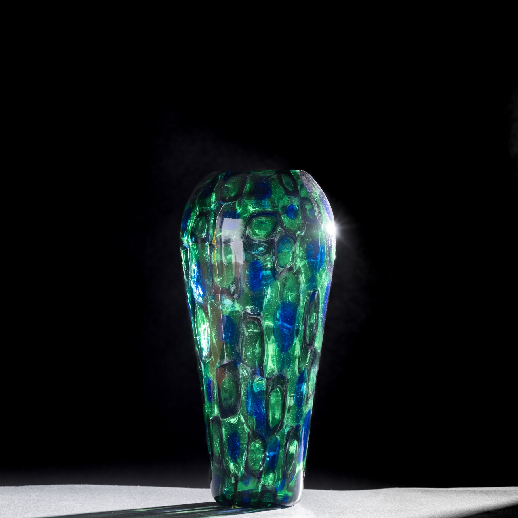 Green and blue patterned glass vase on a dark background