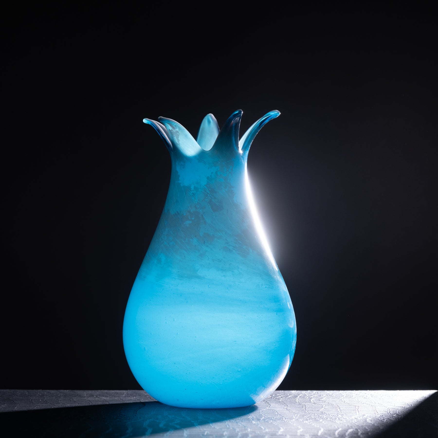 Blue glass vase with a unique design on a black background