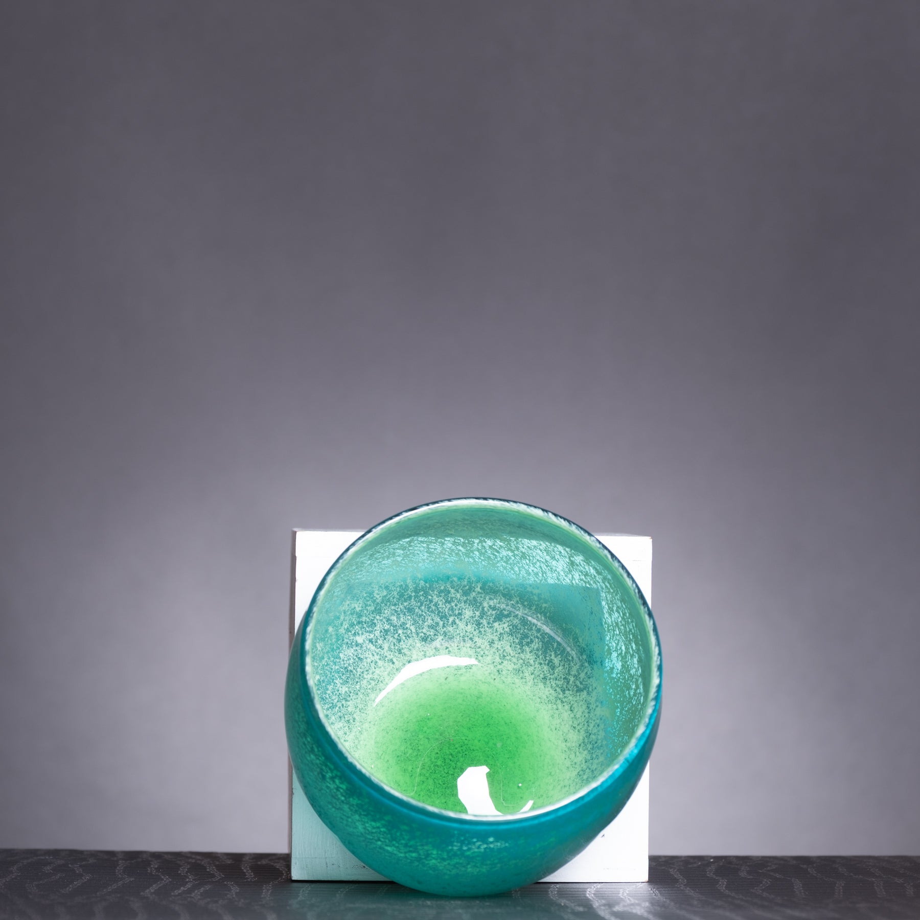 Green candle in a textured glass holder on a dark surface with a gray background