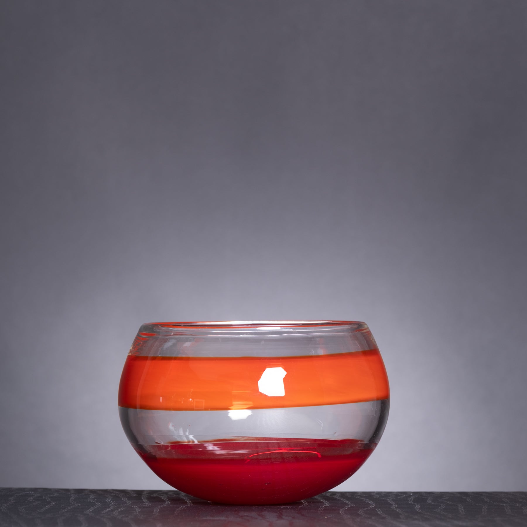 Glass bowl with orange and red stripes on a gray background