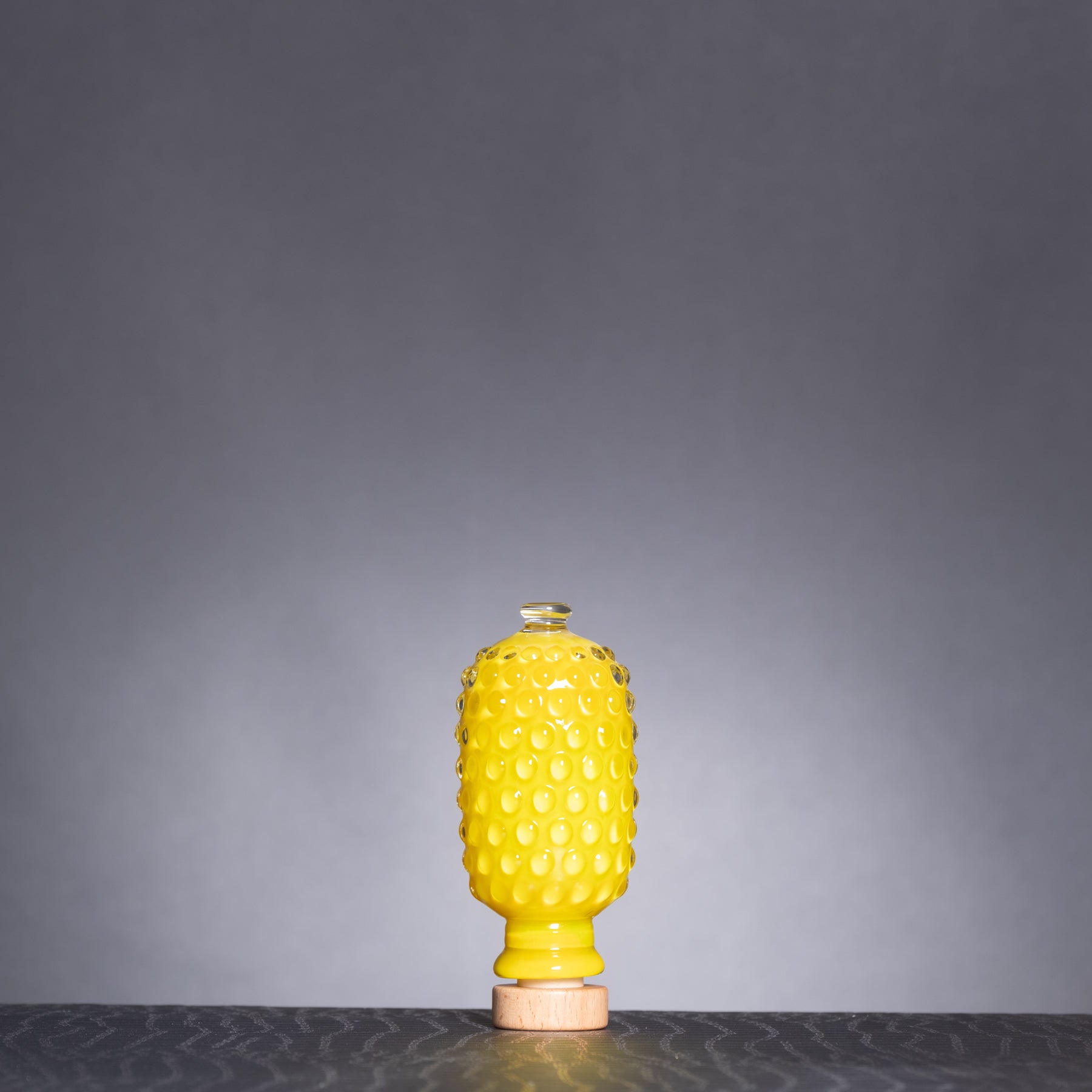Yellow textured bottle with wooden base on a dark surface and gray background